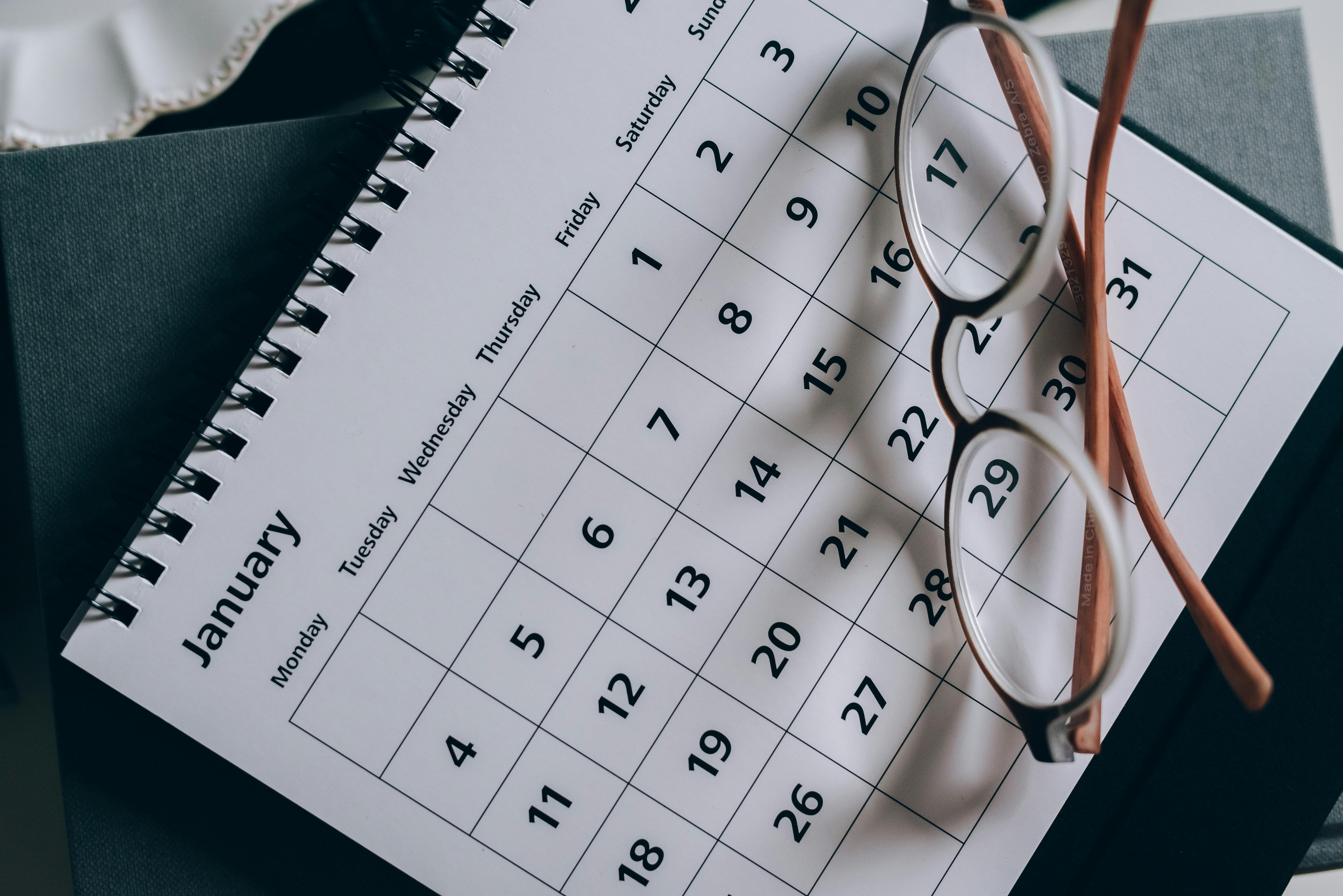 A spiral-bound January calendar lies open with a pair of brown-framed eyeglasses resting on top.