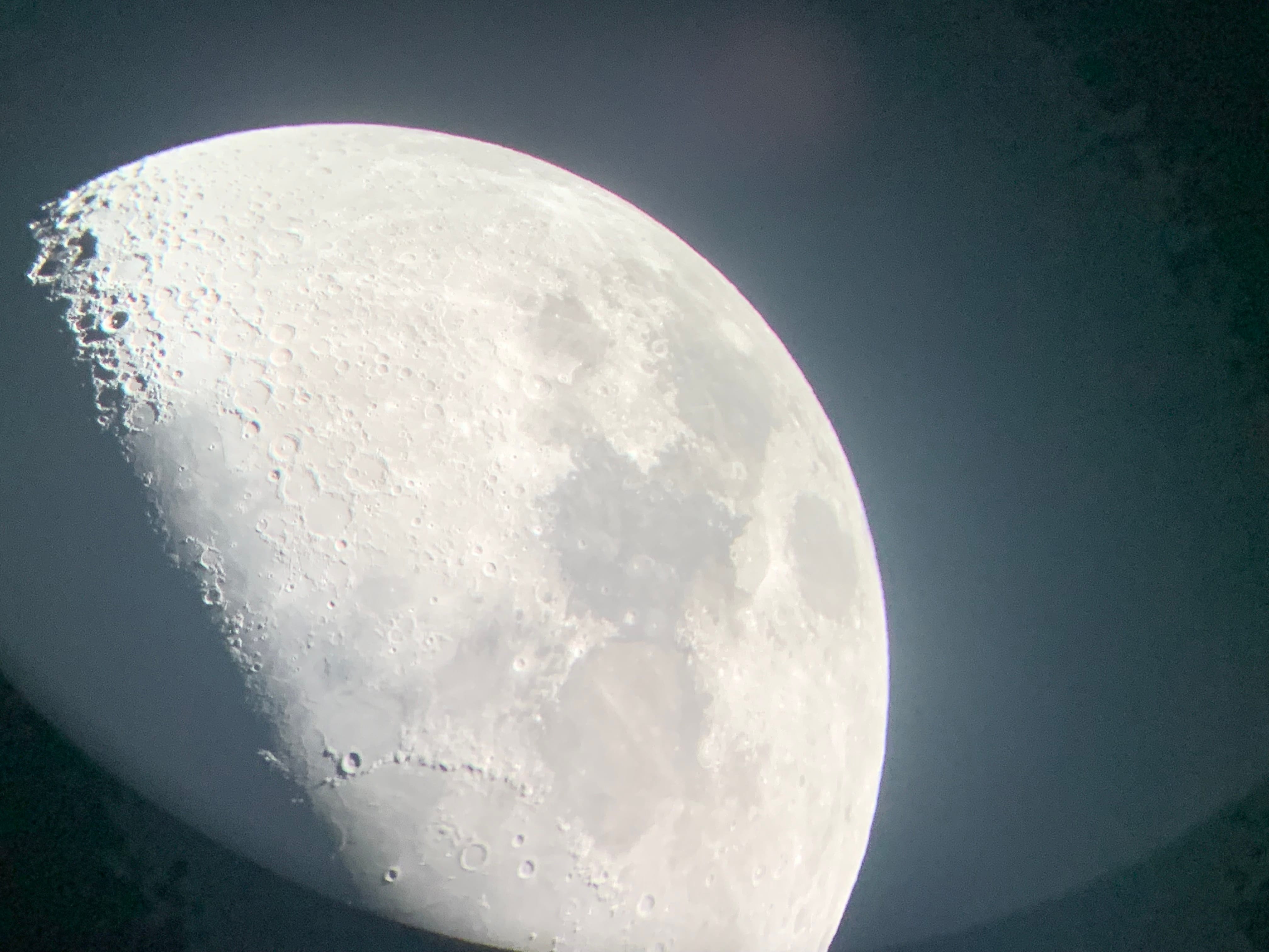 Close-up of the moon showing detailed craters and surface texture against a dark gray sky.