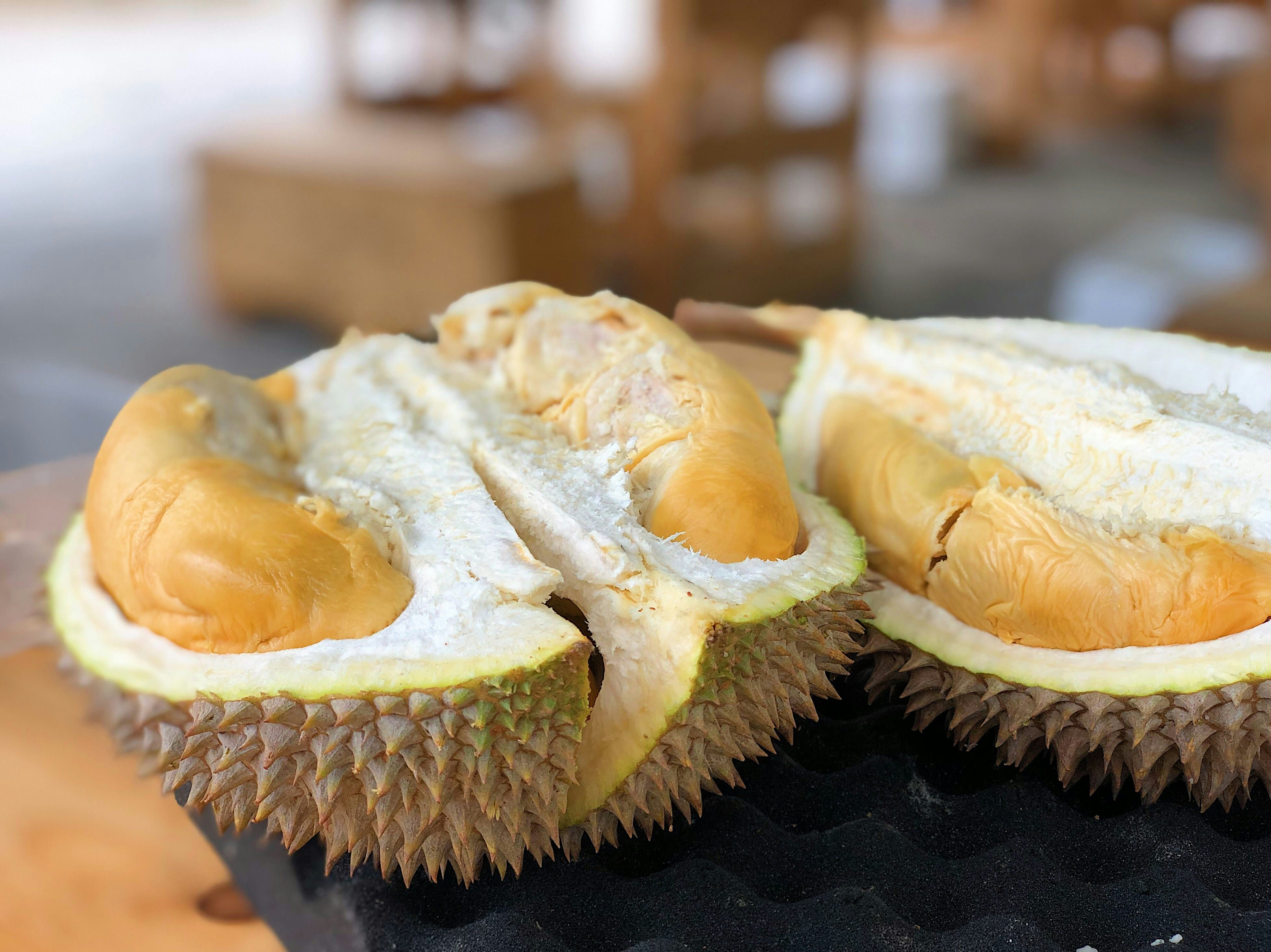 A split-open durian fruit showing yellow-orange flesh pods inside its spiky green-brown shell on a dark surface.