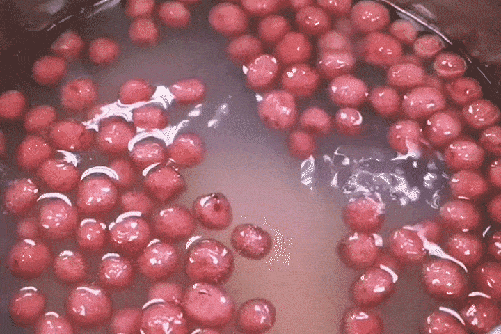 Red cranberries simmering in a pot of liquid, with bubbles visible around the berries.