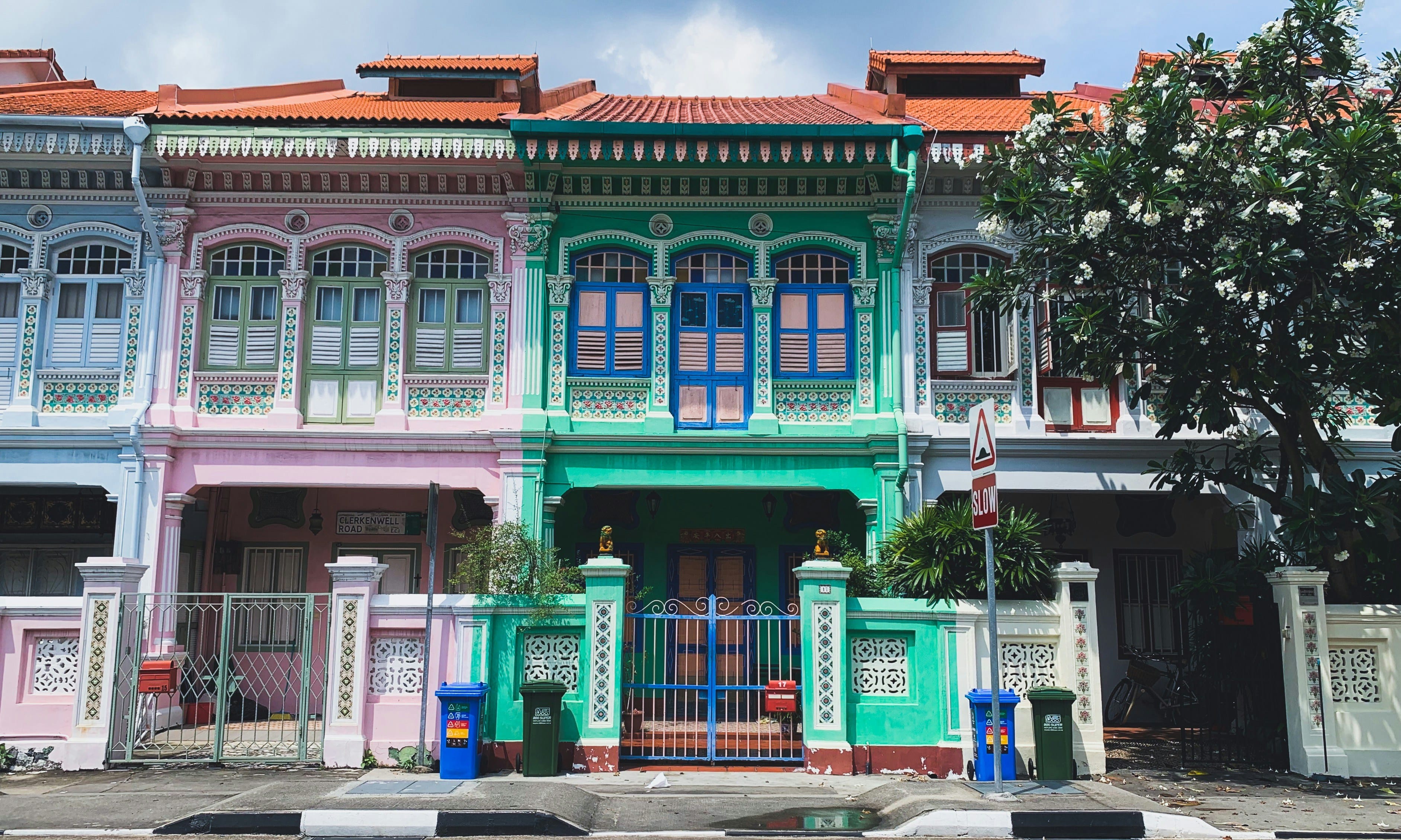 Colorful Peranakan shophouses in pink, teal, and white with ornate facades and red tile roofs on a street.