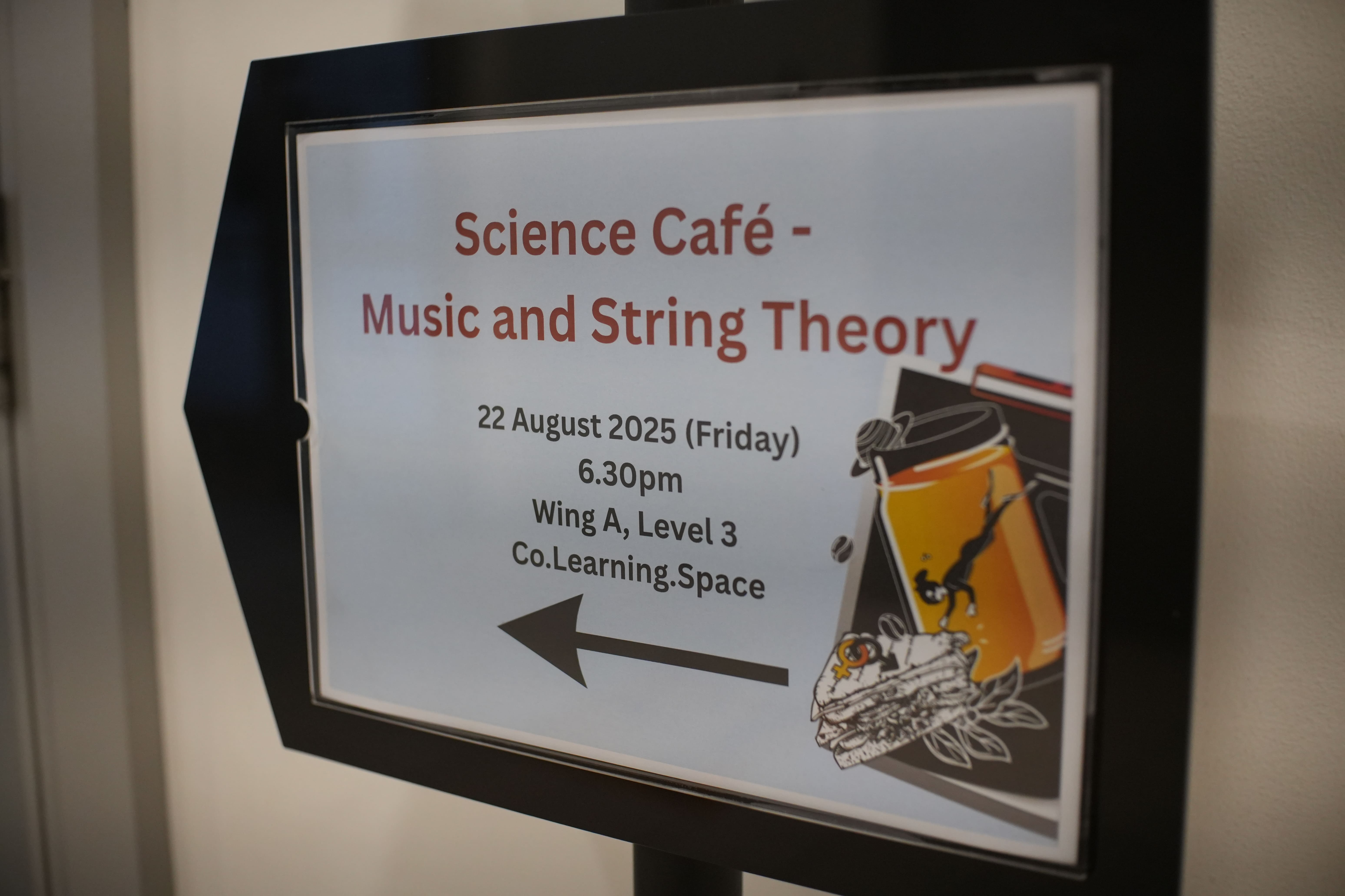 A framed sign reads Science Cafe Music and String Theory, 22 August 2025, 6.30pm, Wing A Level 3, with a left arrow.