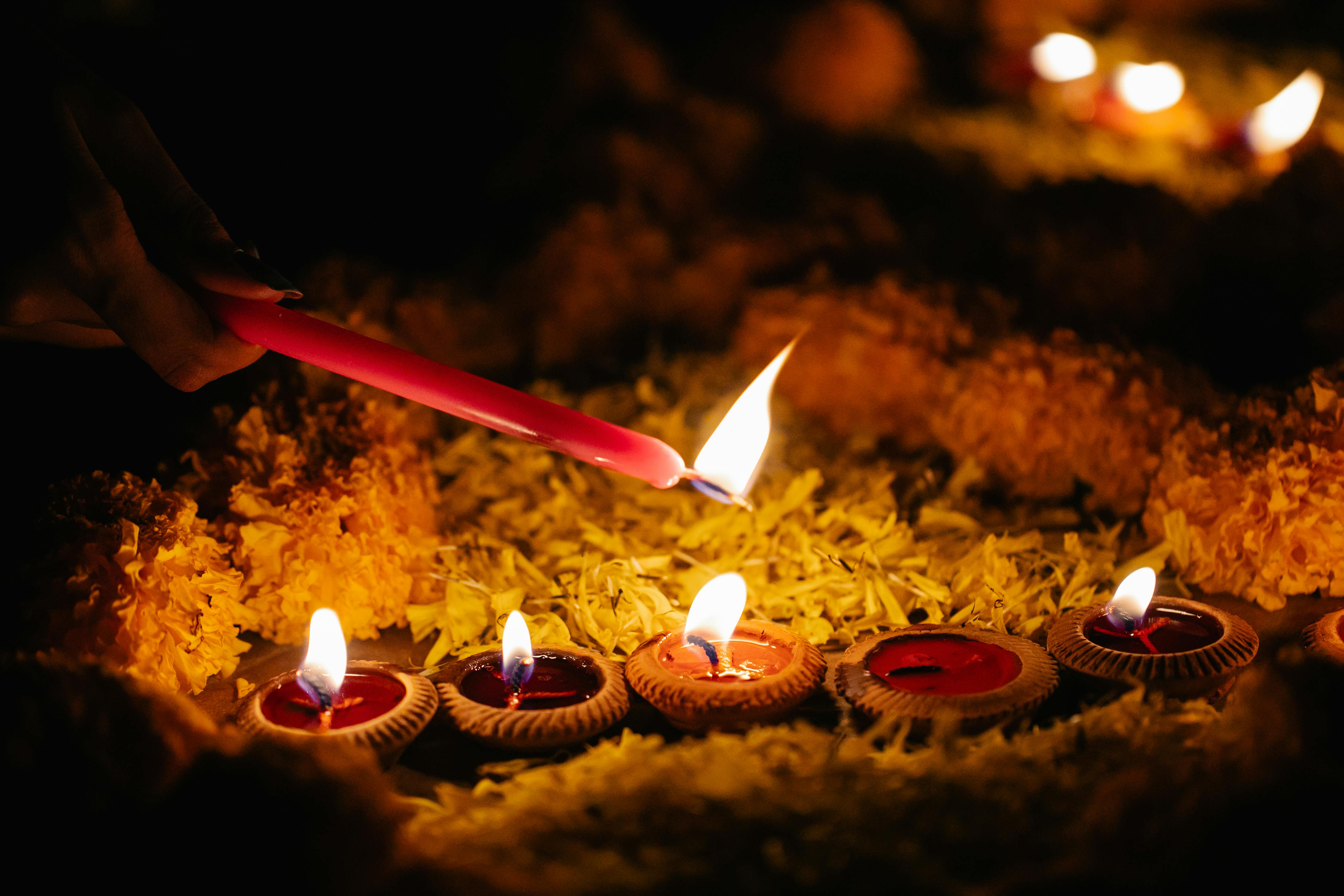 A hand lighting small clay oil lamps arranged on yellow marigold petals in a dark setting.