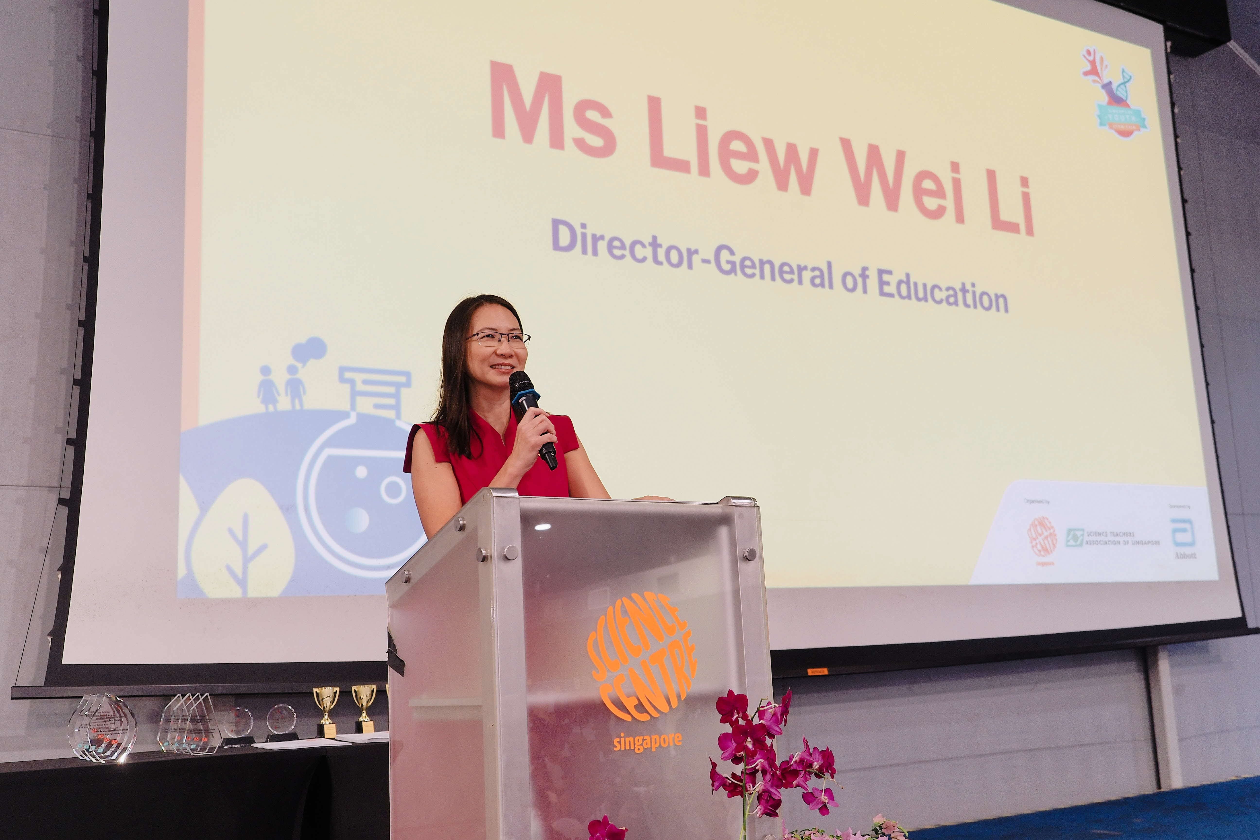 Woman in red dress speaking at a Science Centre Singapore podium, with a slide reading "Ms Liew Wei Li, Director-General of Education."