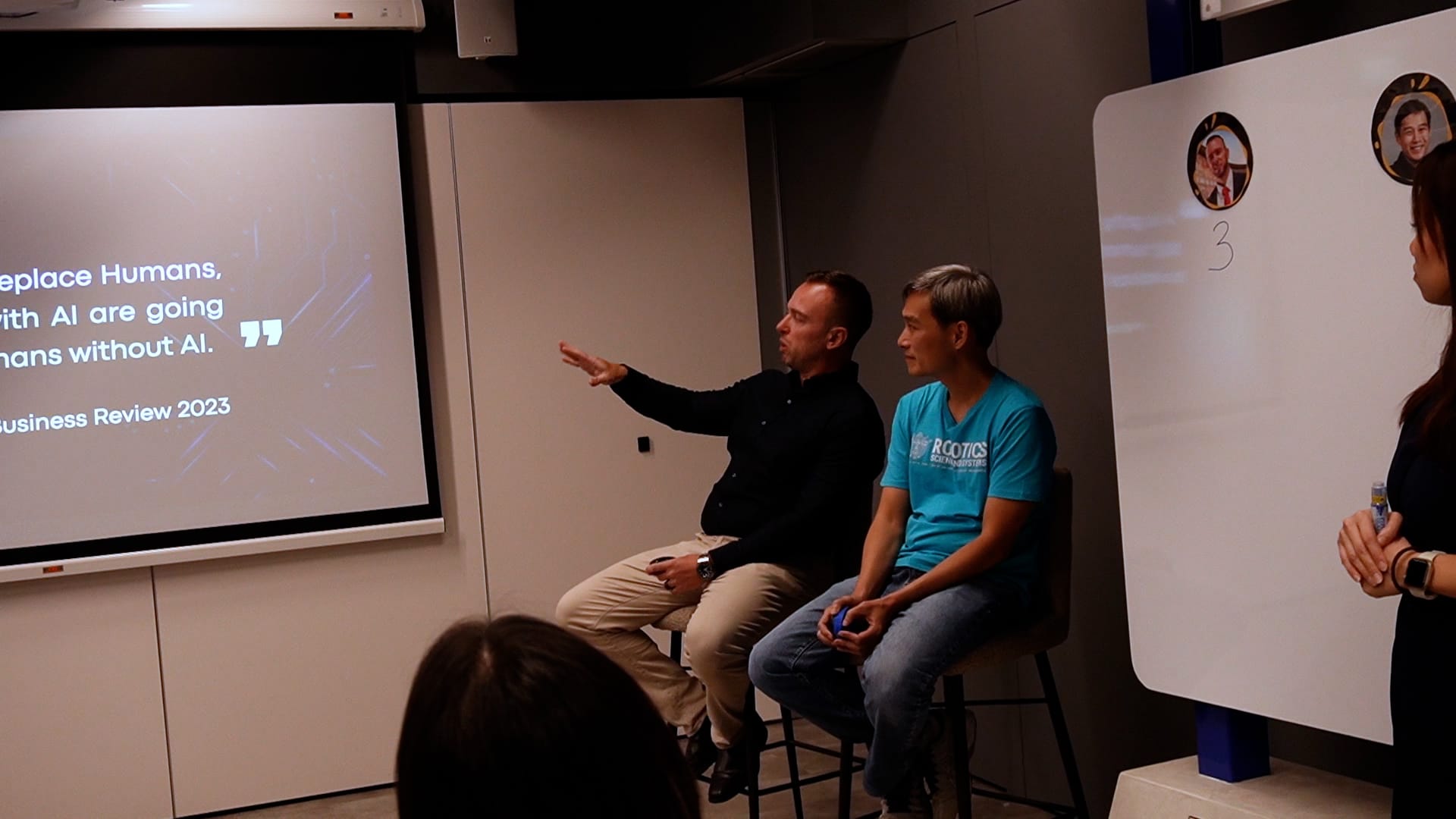 Two men sit on stools during a presentation, with a slide about AI and humans from Harvard Business Review 2023 visible.