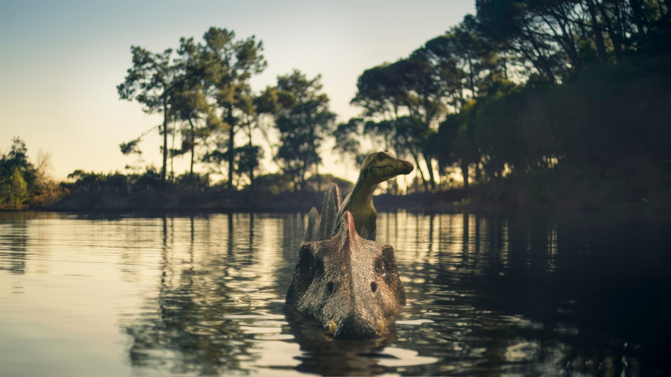Two dinosaur figurines partially submerged in a calm lake, with trees and a pale sky in the background.