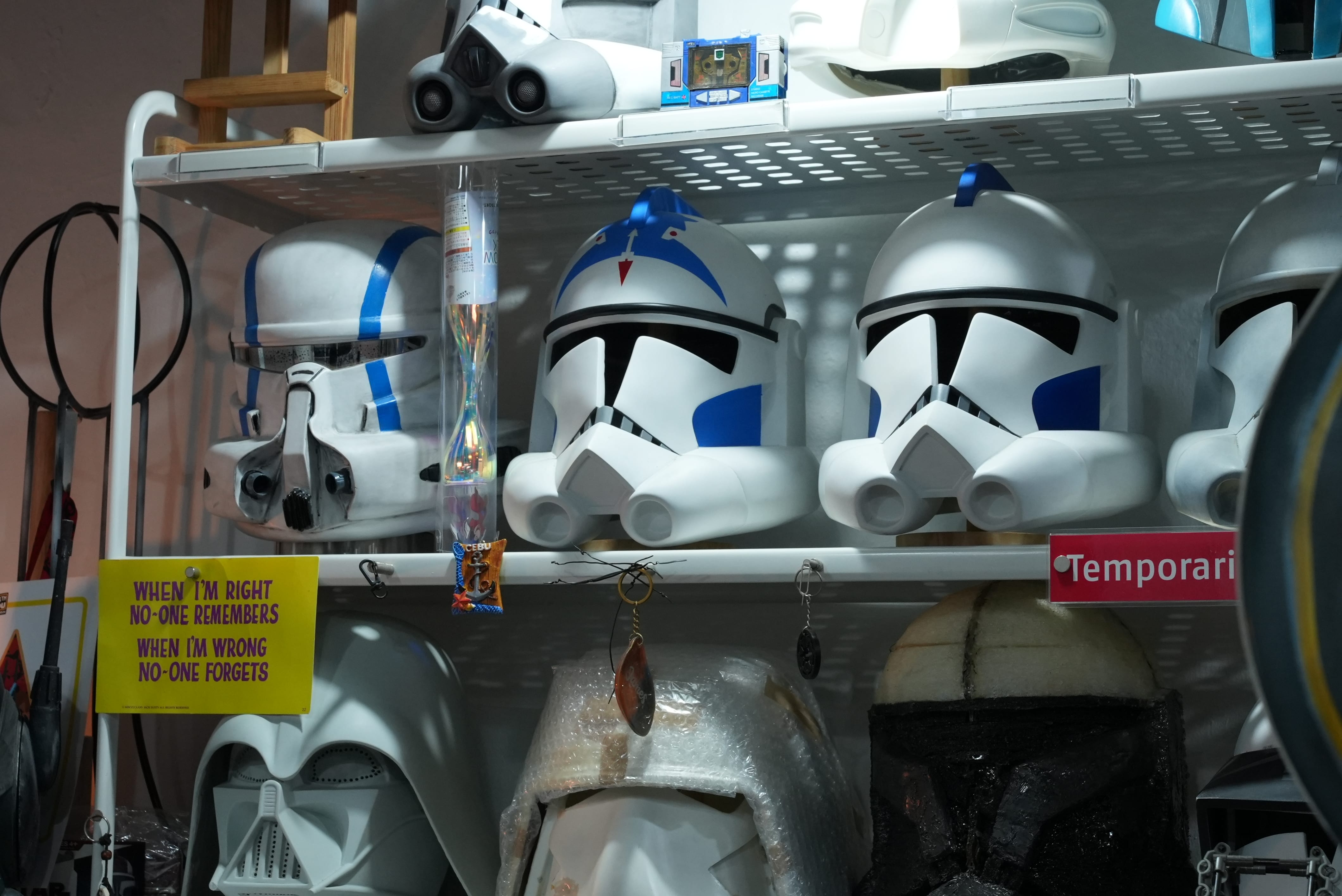 White and blue Star Wars clone trooper helmets displayed on shelves alongside a Darth Vader mask and a yellow novelty sign.