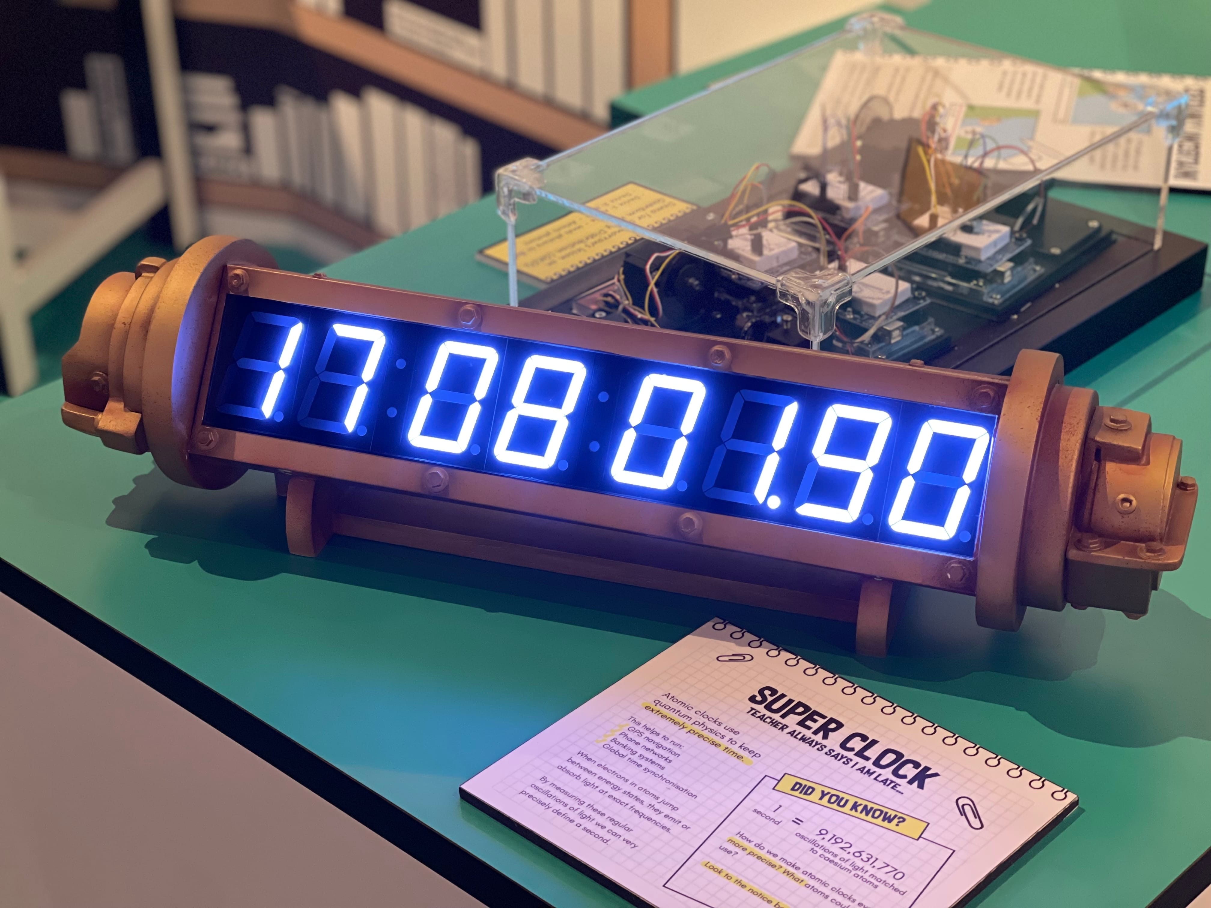 A steampunk-style digital clock displaying 17:08:01.90 in blue LEDs, labeled "Super Clock" on a nearby card.
