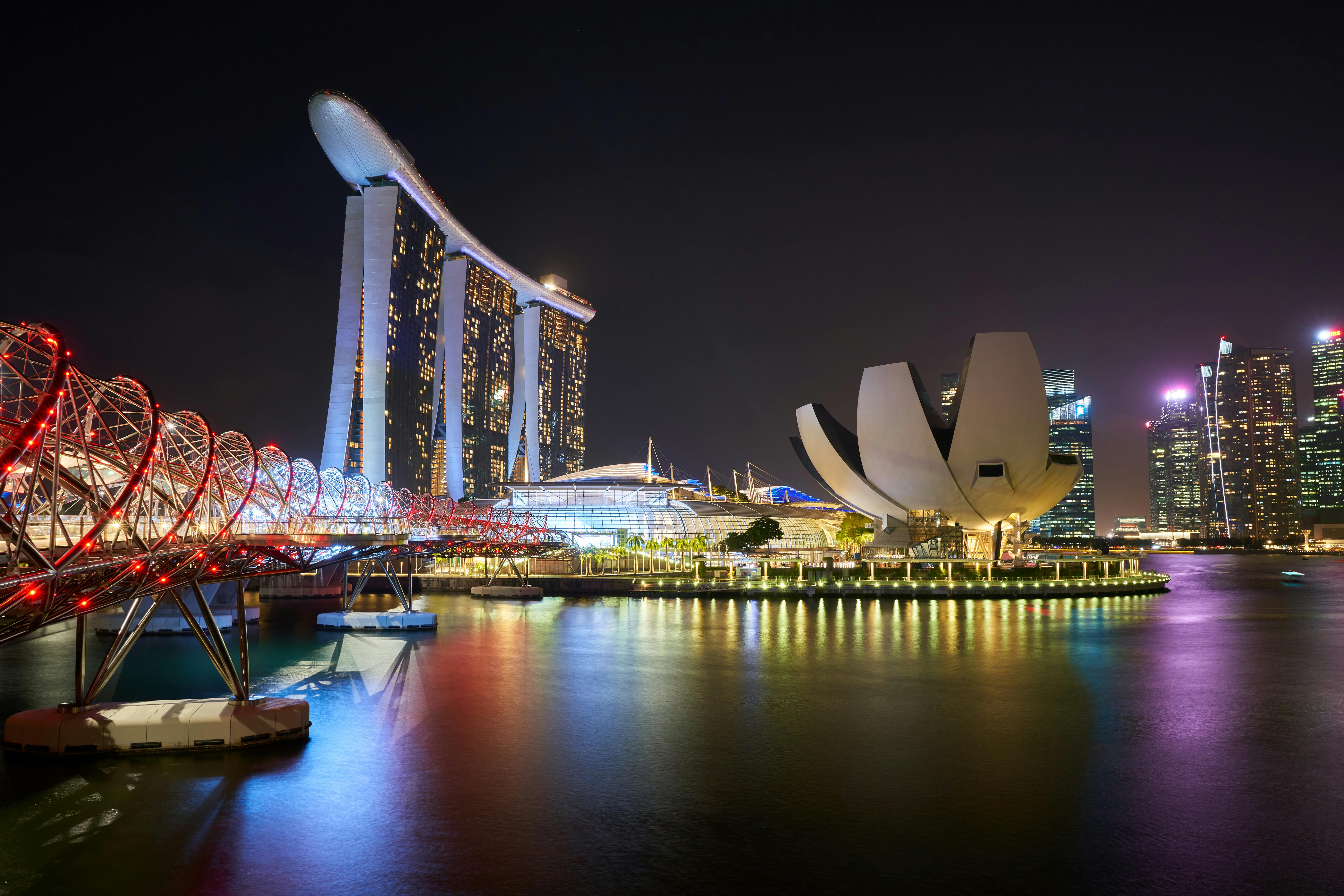 Singapore's Marina Bay at night with the Helix Bridge, Marina Bay Sands towers, and ArtScience Museum reflected in water.