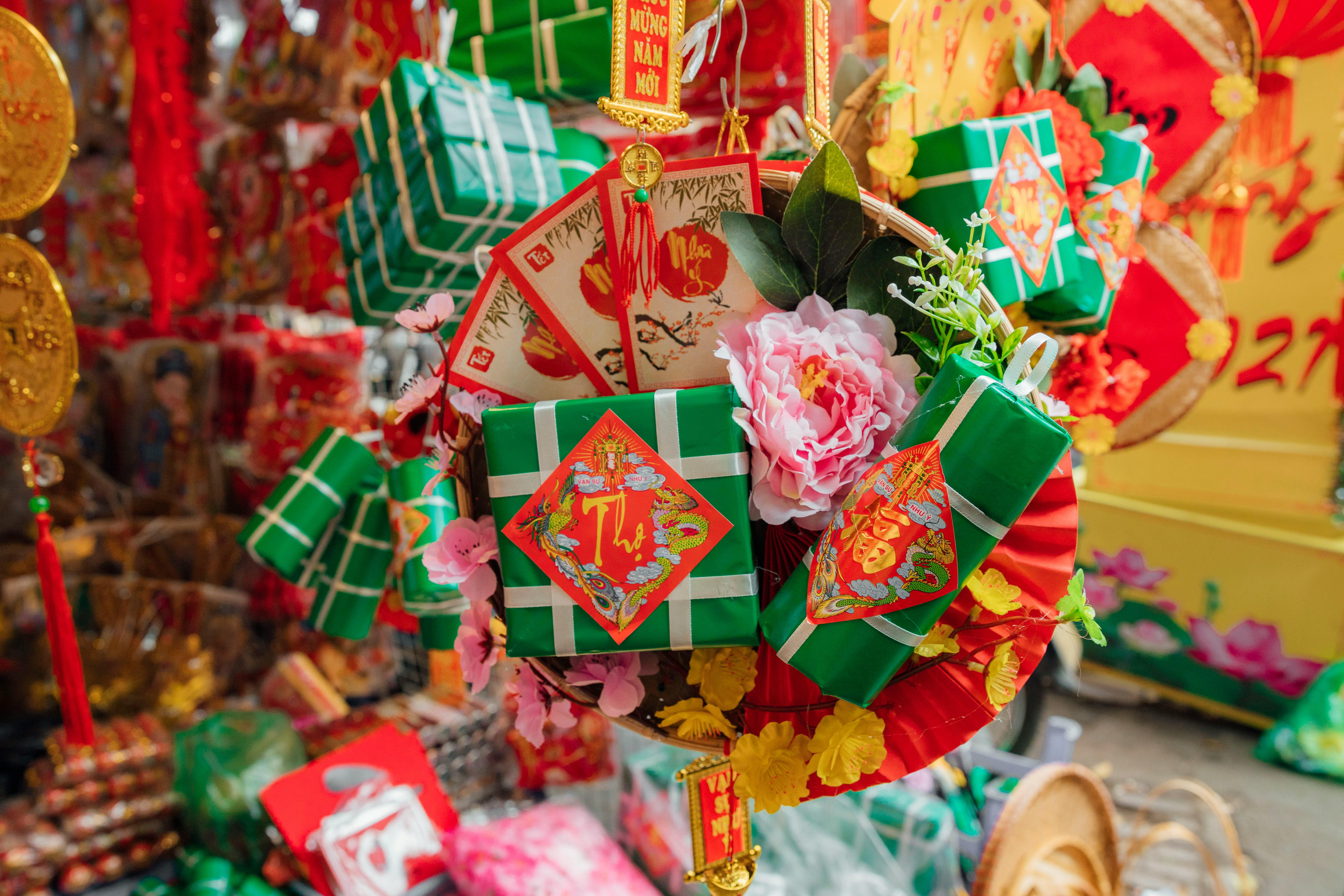 Green gift boxes with red decorative labels, pink flowers, and colorful Vietnamese Lunar New Year decorations displayed at a market.