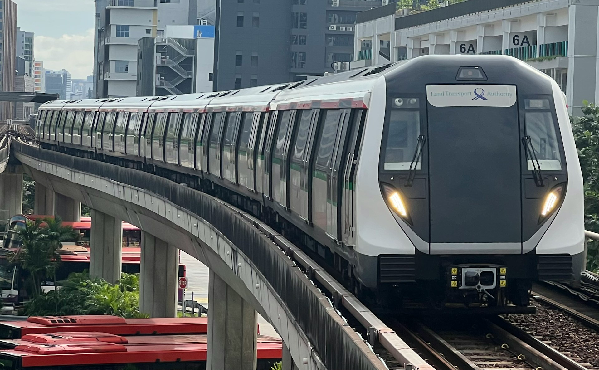 A white and grey Land Transport Authority MRT train on an elevated track curving through a city.