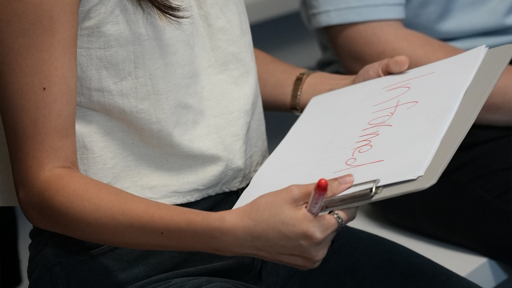 A woman holds a clipboard with red handwritten cursive text on white paper while holding a red-tipped pen.