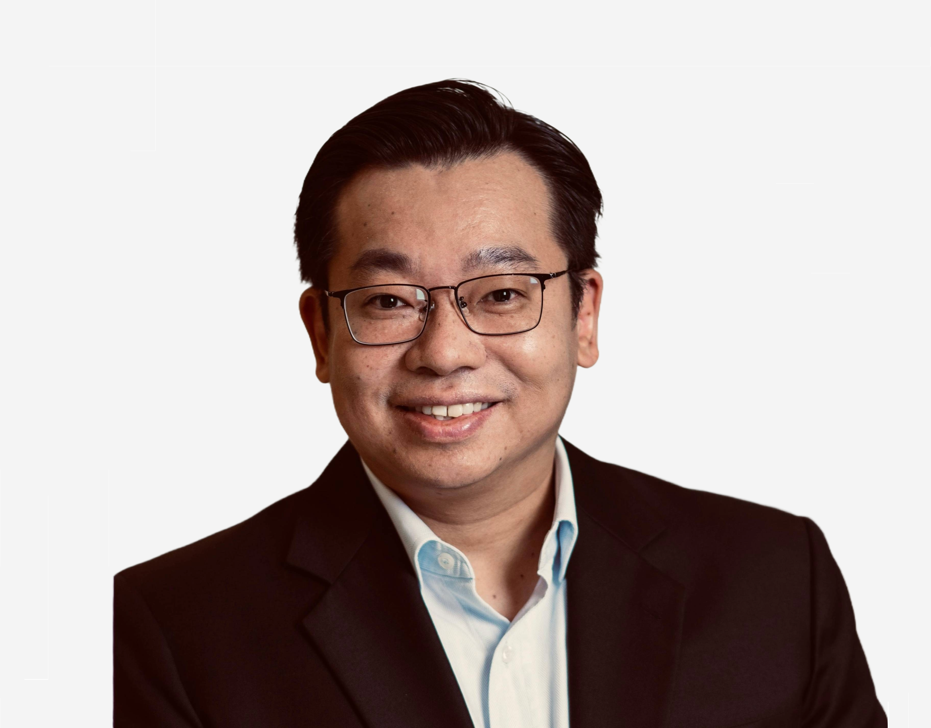 A smiling man in a shirt and black jacket against a light grey background