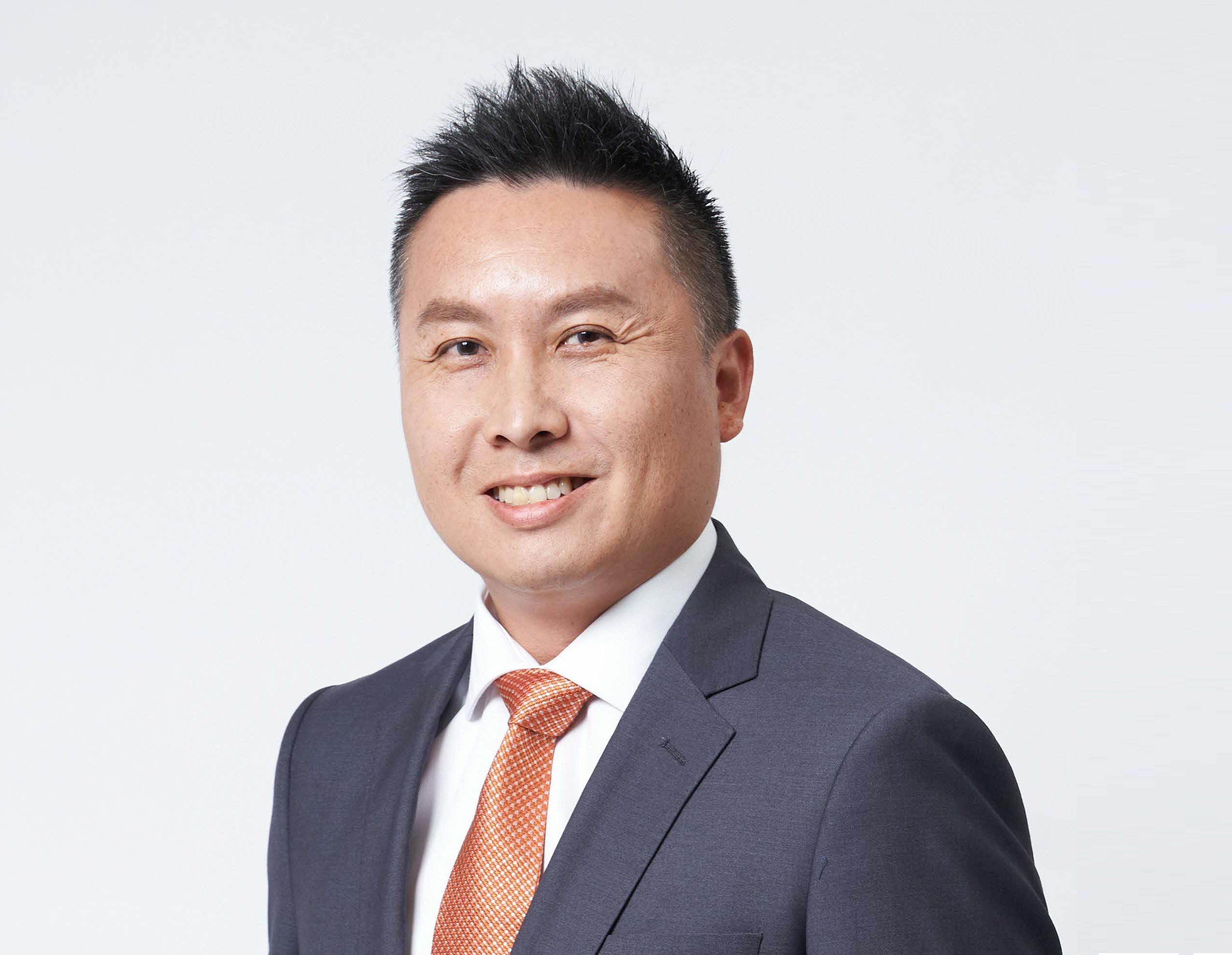 Smiling man with orange tie and suit against light background