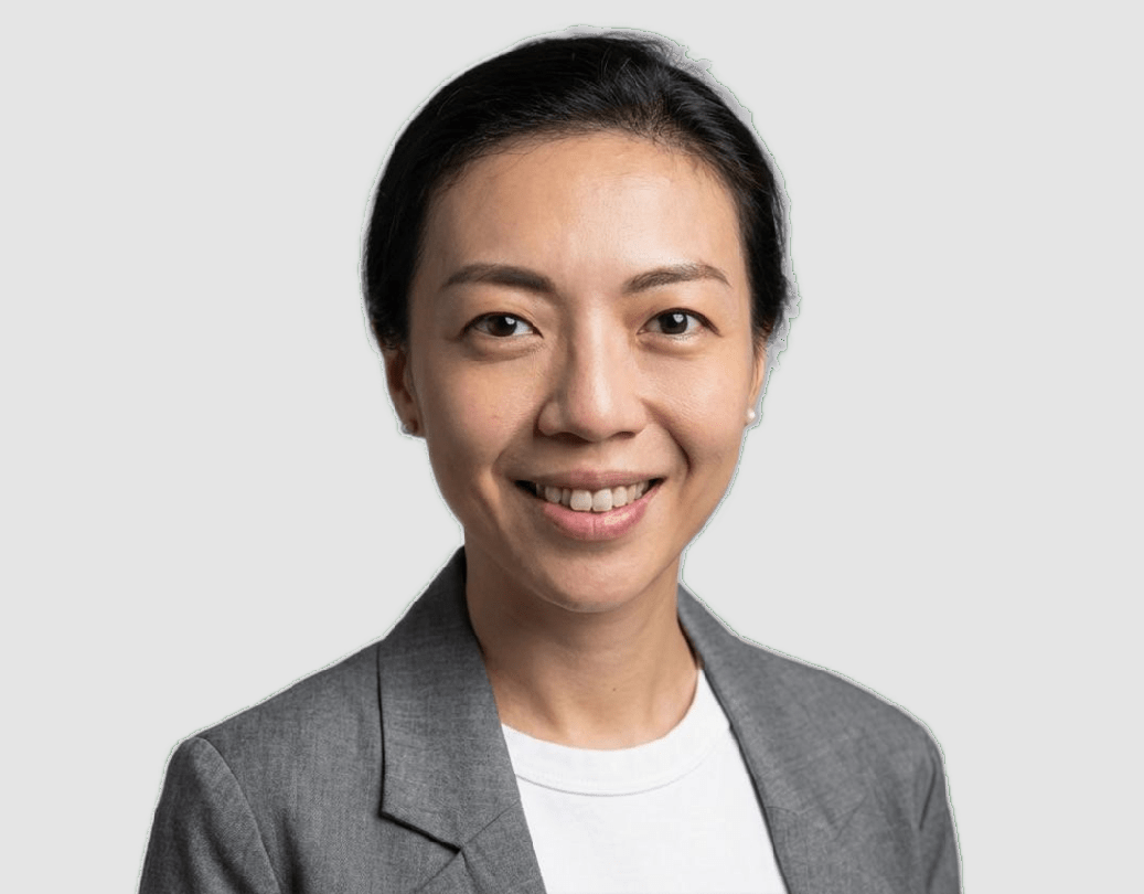 A smiling woman with dark hair pulled back, wearing a gray blazer over a white top, against a light gray background.
