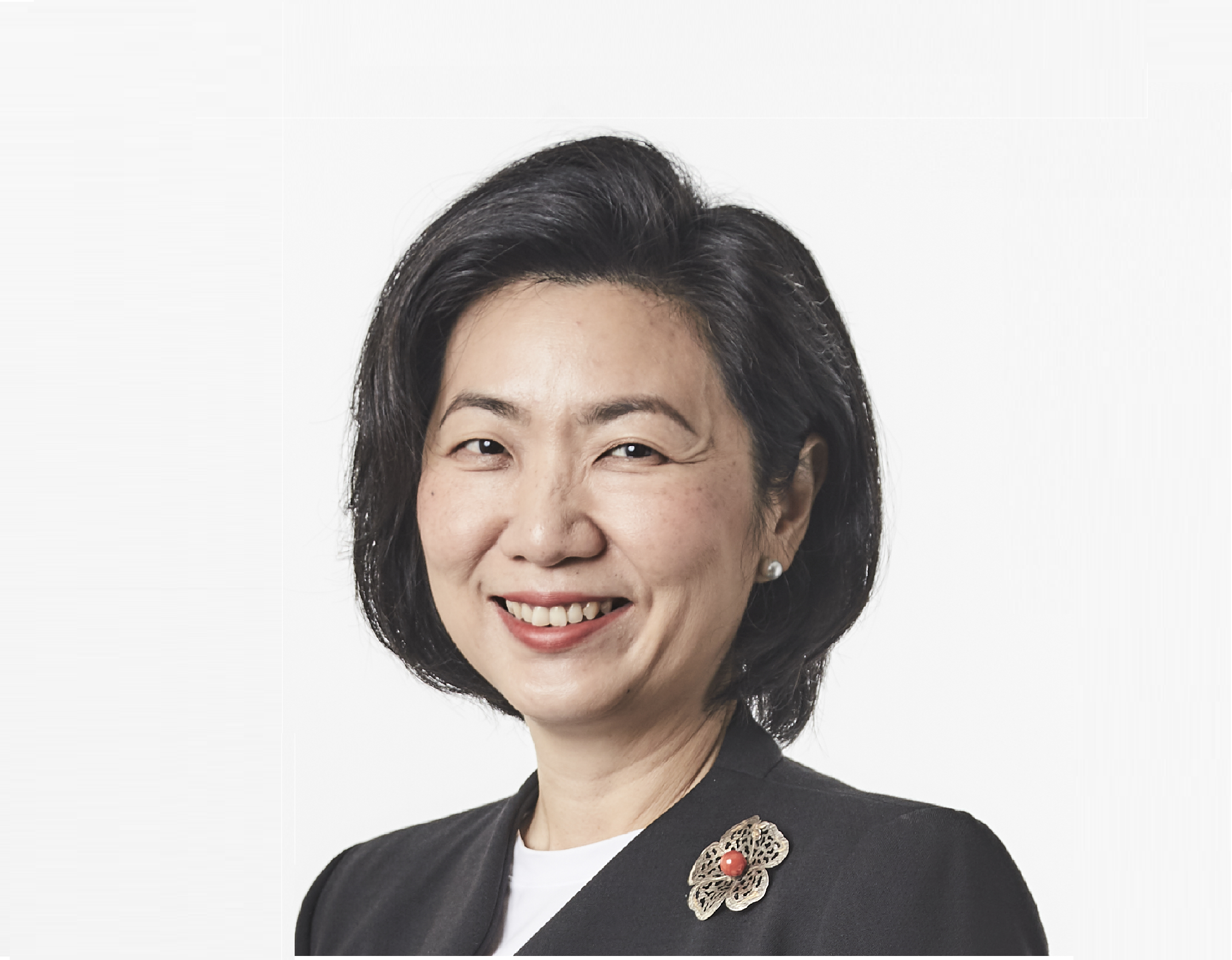 A smiling middle-aged woman with short dark hair, pearl earring, and a black blazer with a floral brooch.