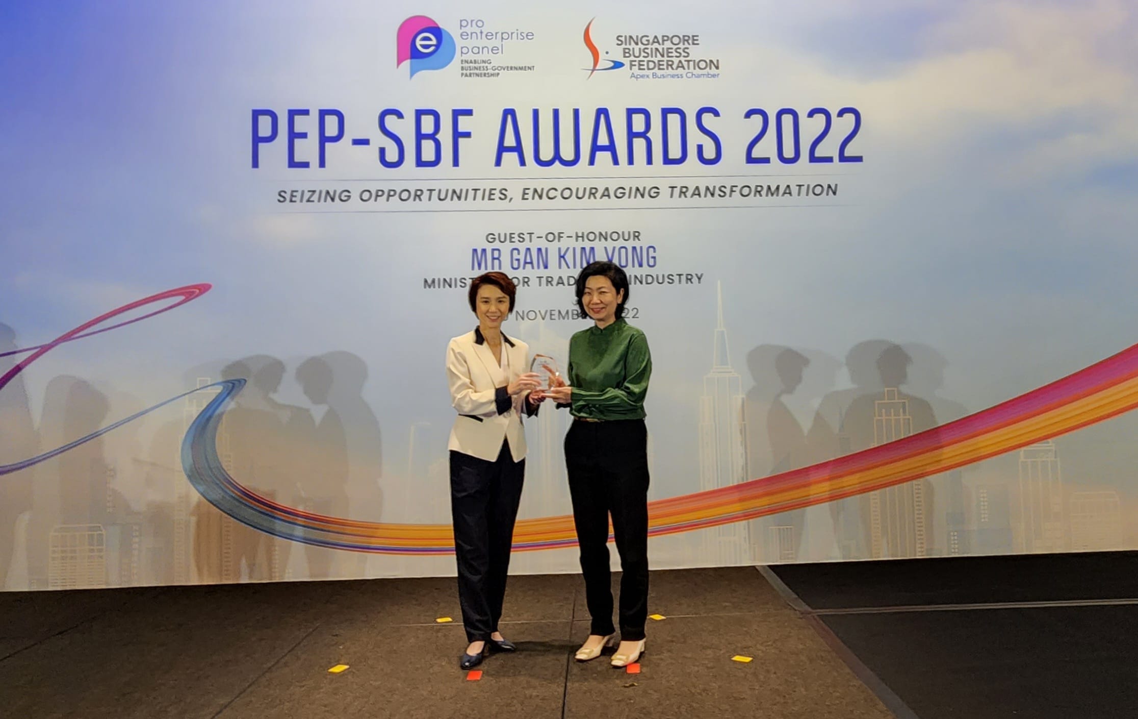 Two women hold a crystal trophy together in front of the PEP-SBF Awards 2022 backdrop in Singapore.