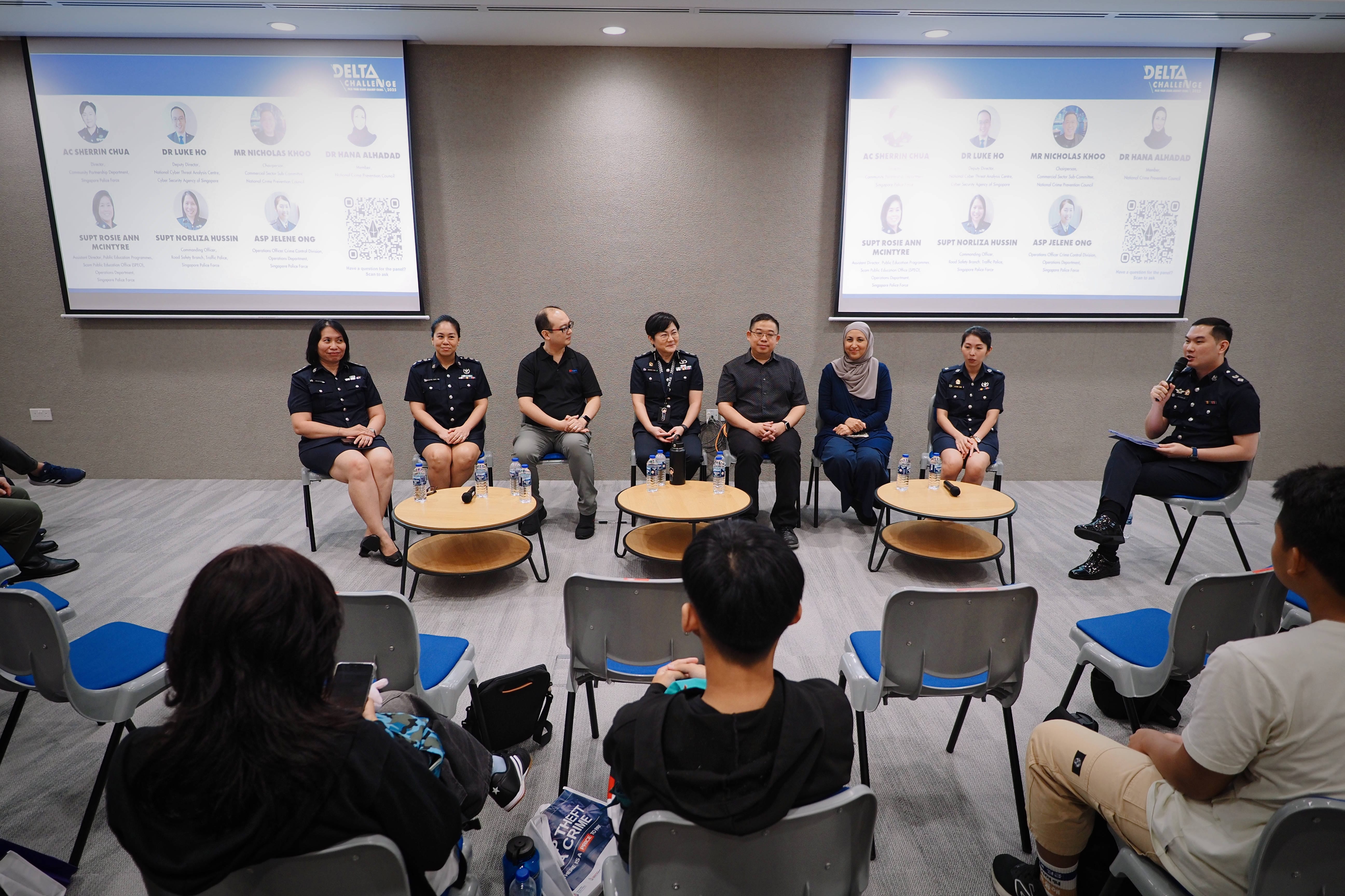 Eight panelists seated in a row facing an audience at a Delta Challenge event, with two projection screens behind them.