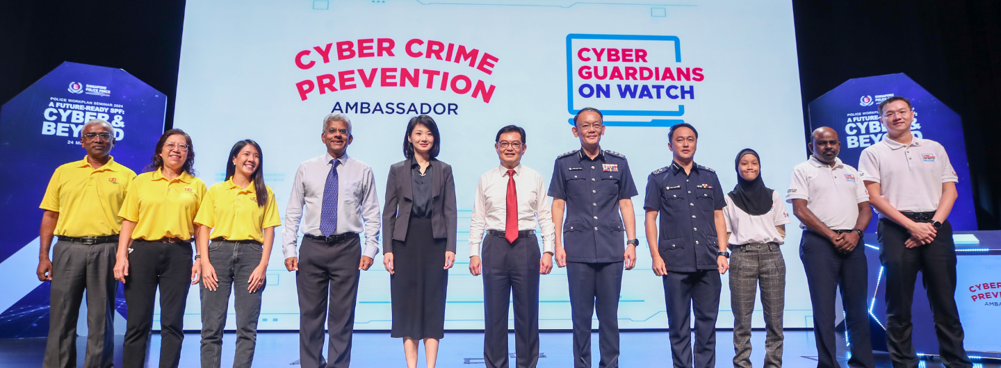 Ten people pose on stage in front of a screen reading Cyber Crime Prevention Ambassador and Cyber Guardians on Watch.