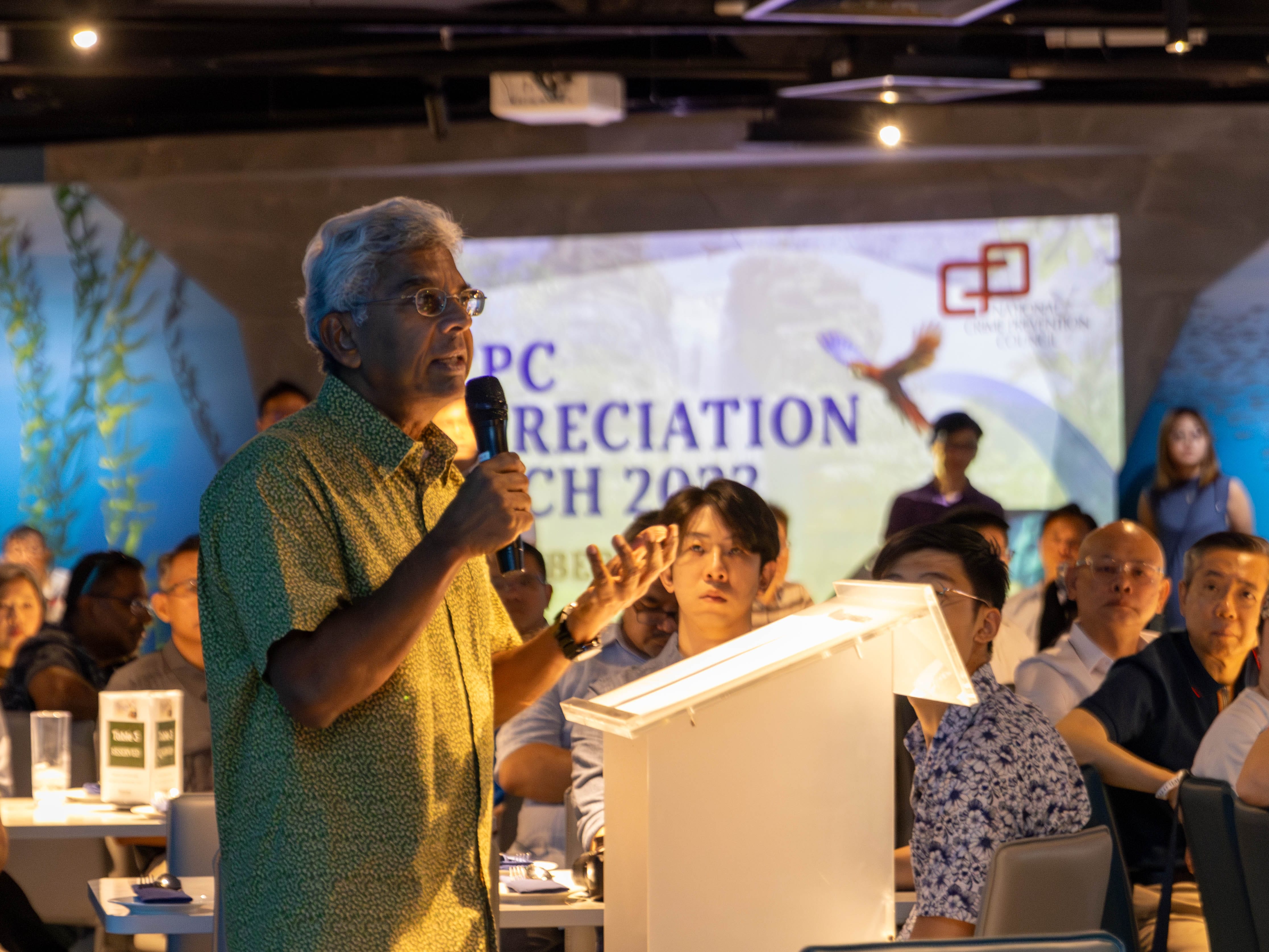 Mr Gerald Singham speaks into a microphone at a podium before a seated audience at a 2022 event.