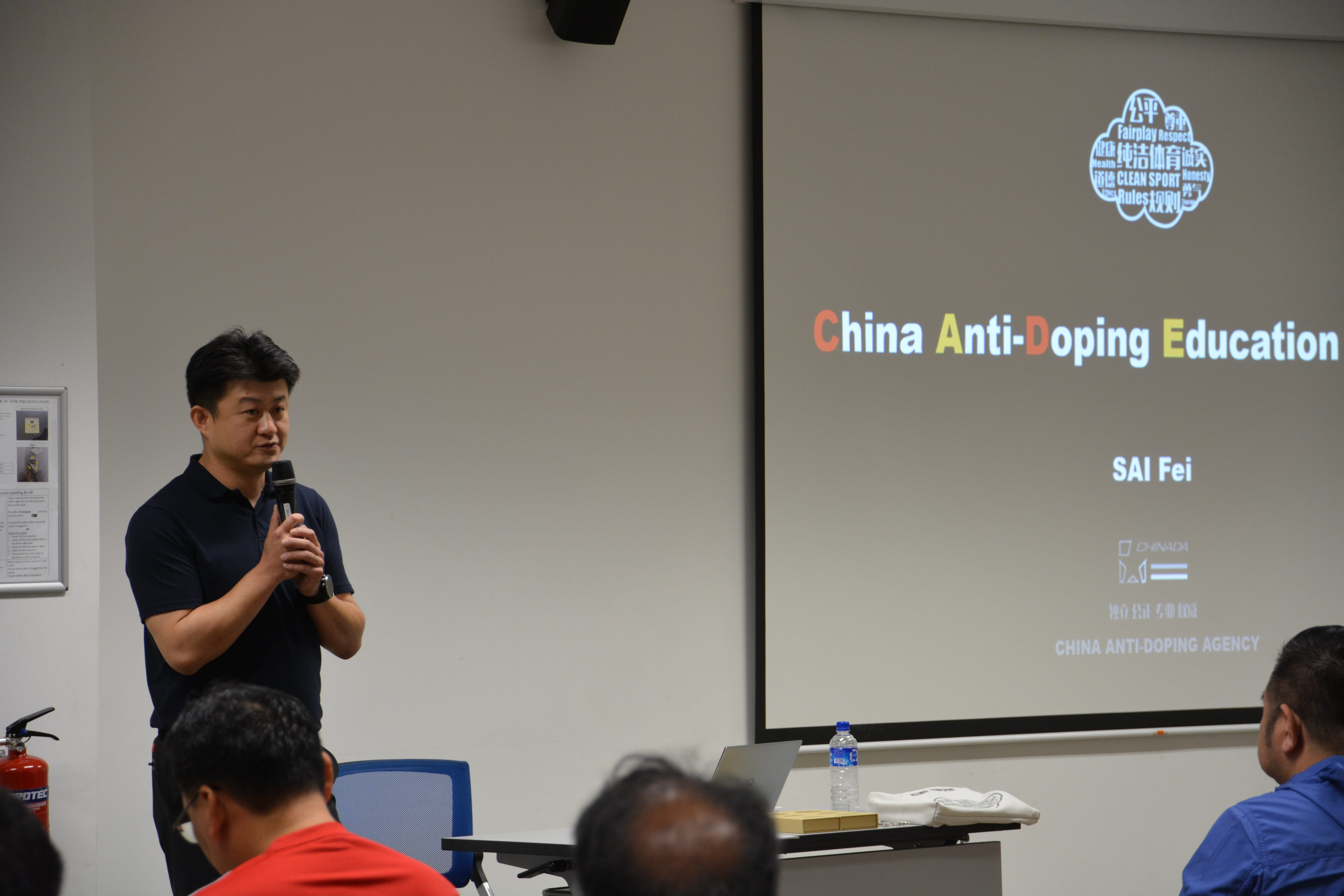 Presenter with blurred face speaks into a microphone beside a slide reading China Anti-Doping Education.