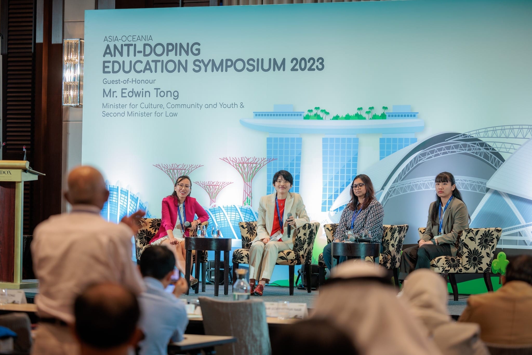 Four panelists seated on stage at the Asia-Oceania Anti-Doping Education Symposium 2023 with a Singapore-themed backdrop.