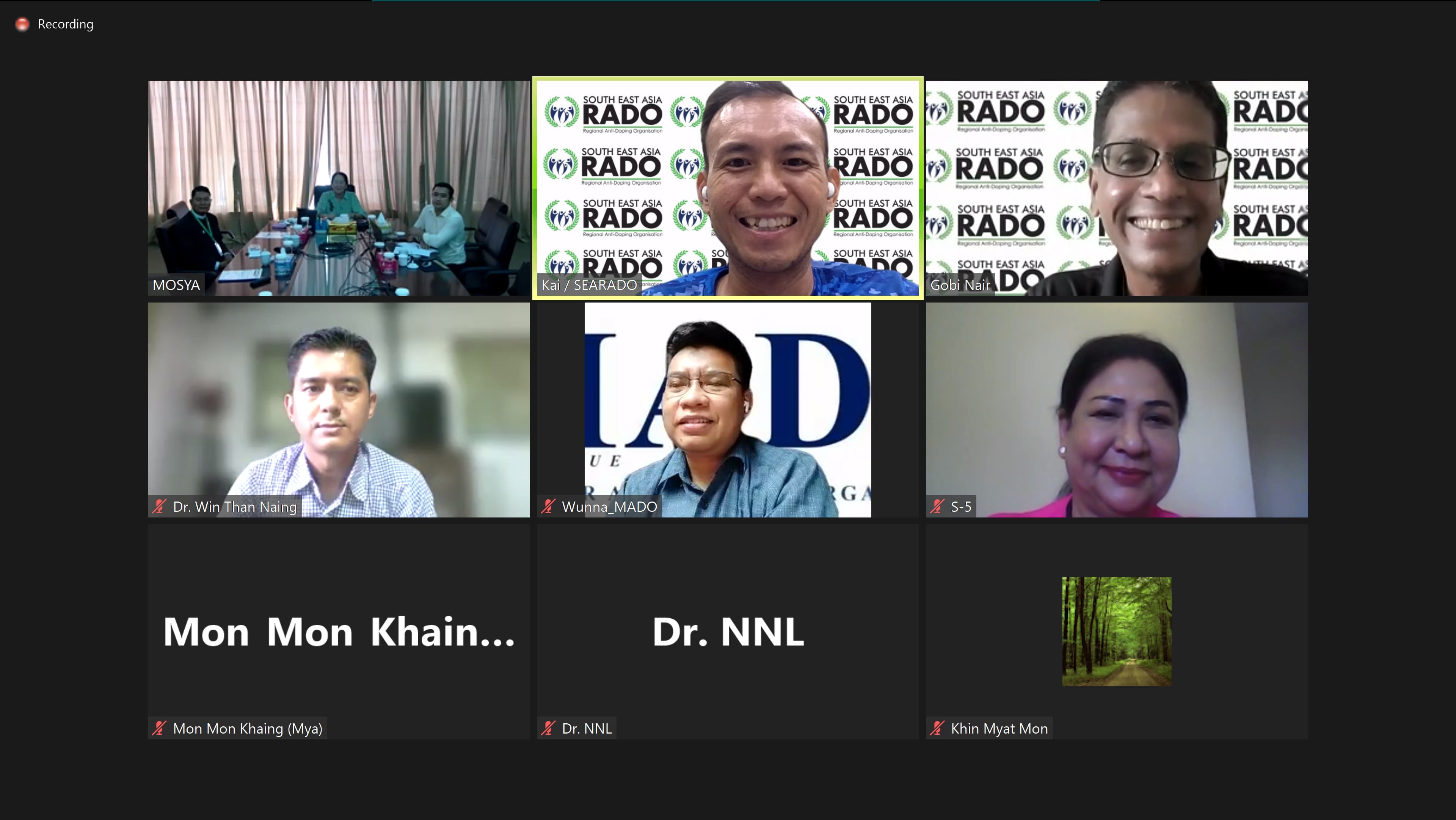 Video call with nine labeled participants, some showing faces and others displaying name text or a forest thumbnail.