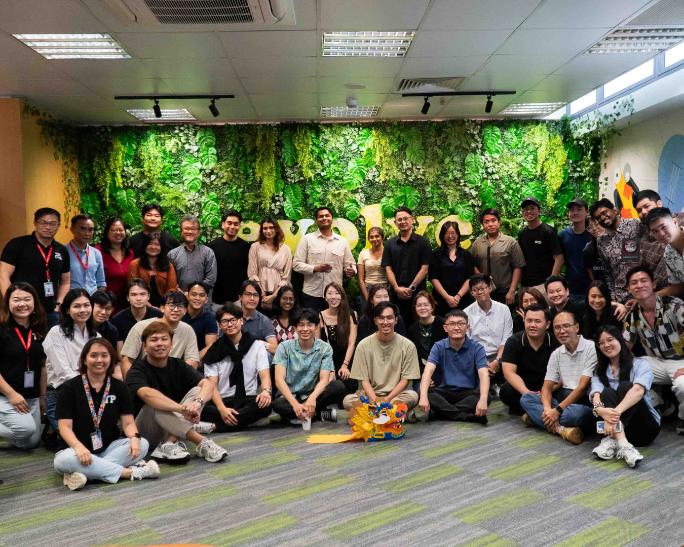 A large group of people posing indoors in front of a green plant wall with the word "evolve" on it.
