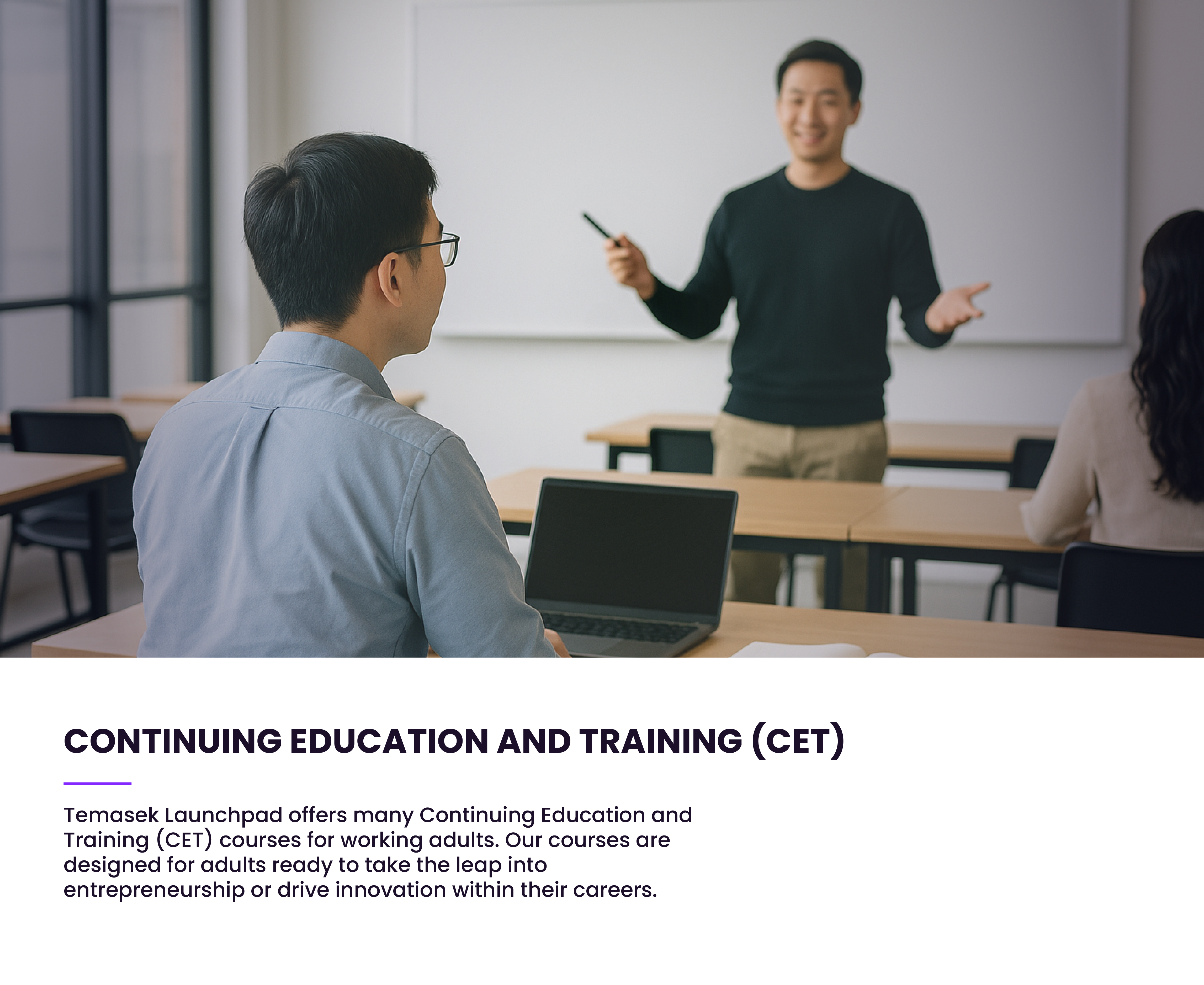 A smiling instructor stands at a whiteboard gesturing, while two students sit at desks in a classroom.