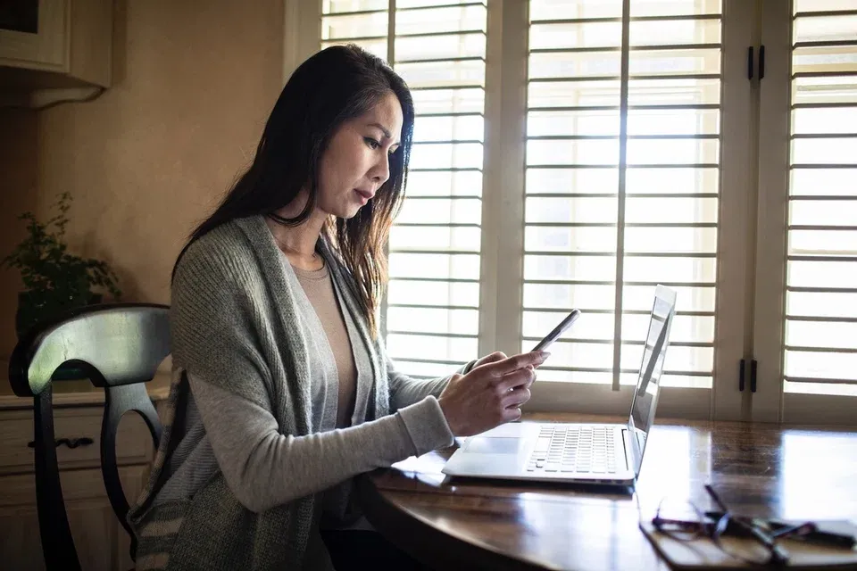 Woman using a mobile phone and laptop at home.