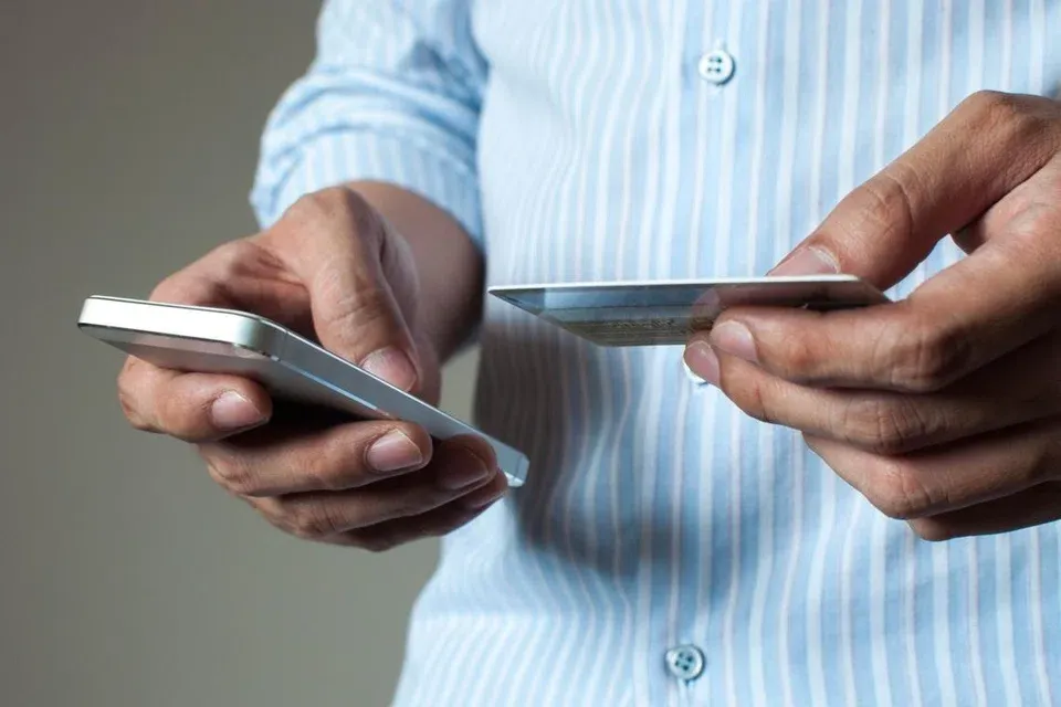 Person holding a mobile phone and bank card while making an online transaction.