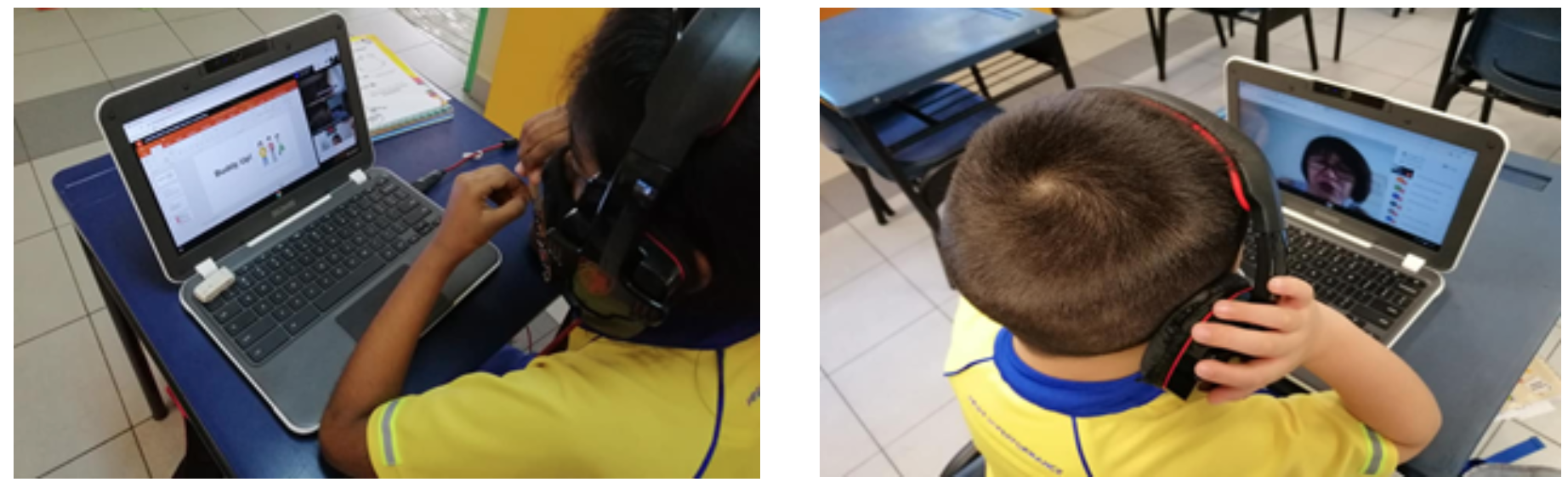 Two children wearing headphones sit at school desks, each using a laptop for a video lesson in a classroom.