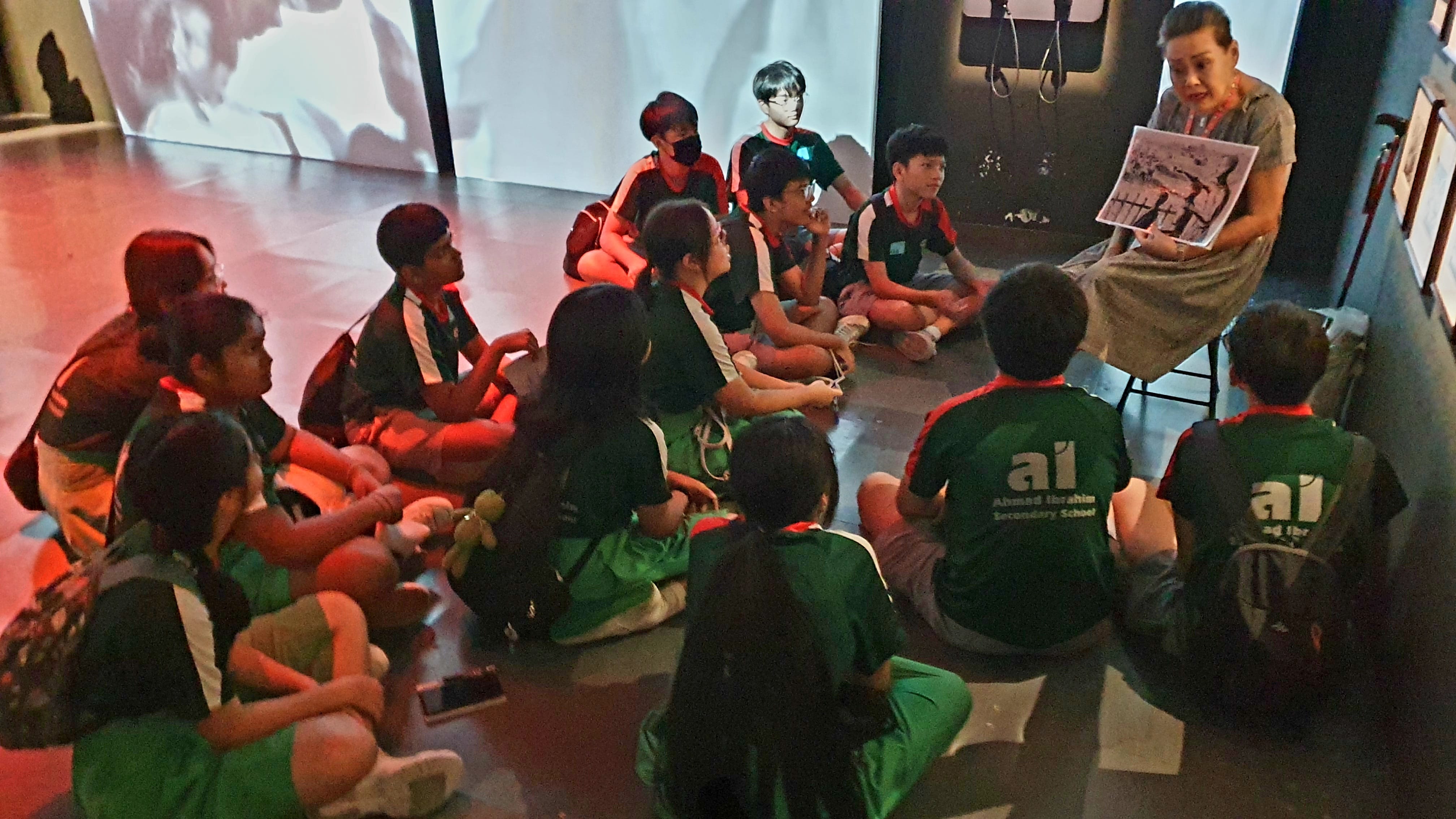 Ahmad Ibrahim Secondary School students sit on the floor as a woman holds up a photograph during a museum talk.