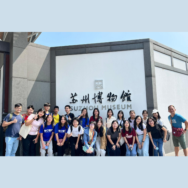 A large group of young people posing in front of the Suzhou Museum entrance sign on a sunny day.