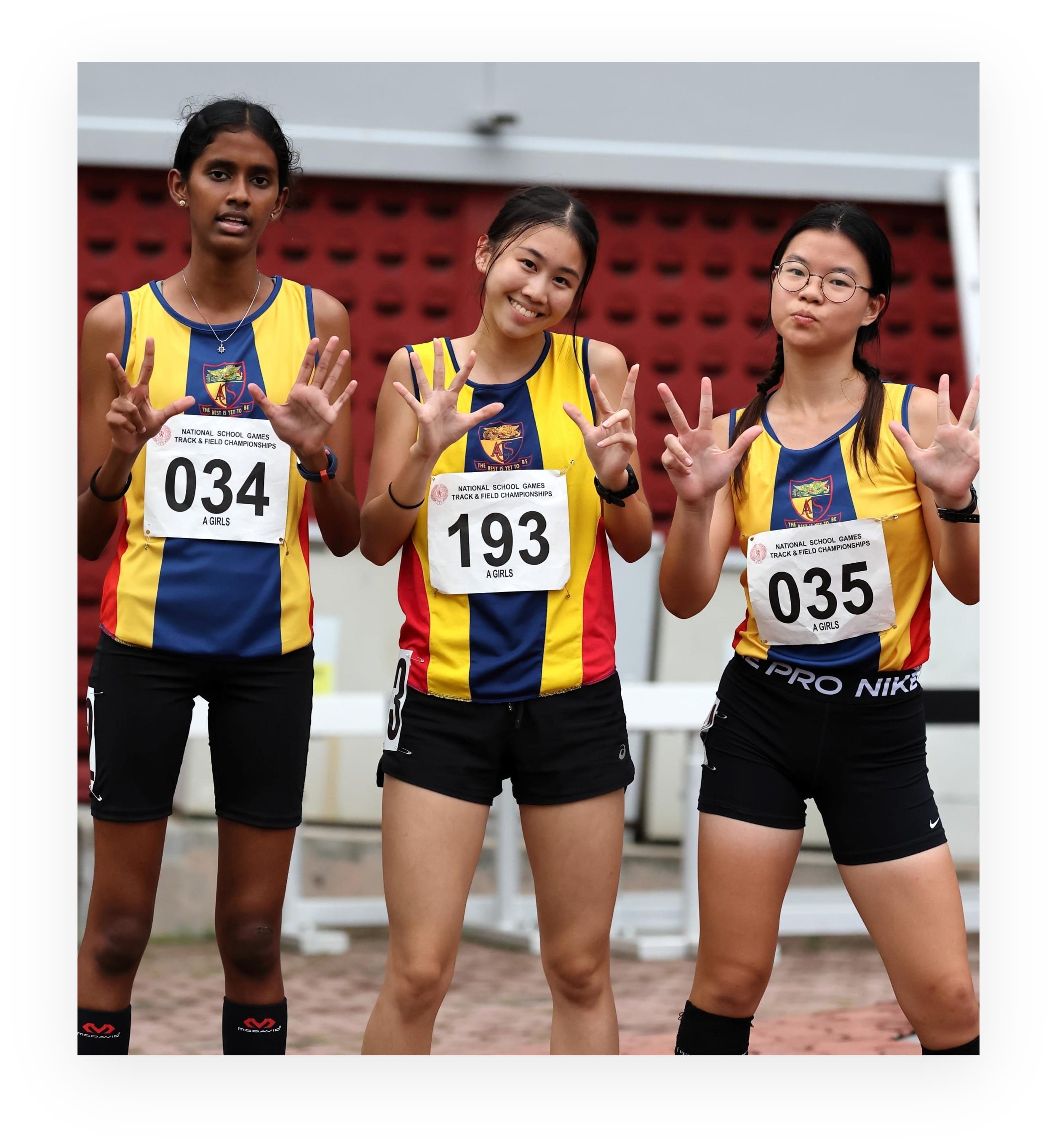 Three girls in matching yellow and blue track uniforms with race bibs 034, 193, and 035 pose at a track meet.