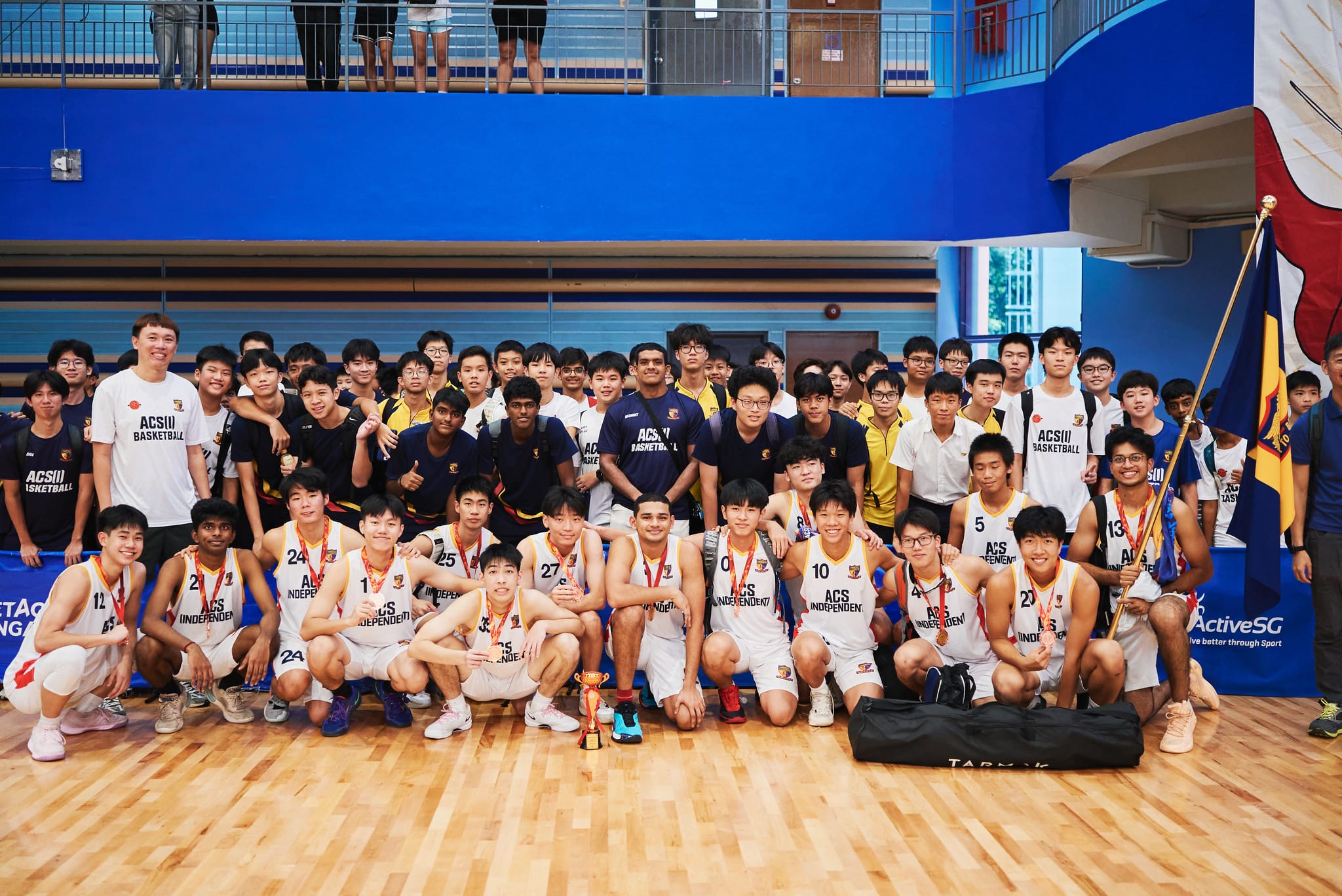 ACS Independent basketball team poses with medals and a trophy on an indoor court after a tournament.