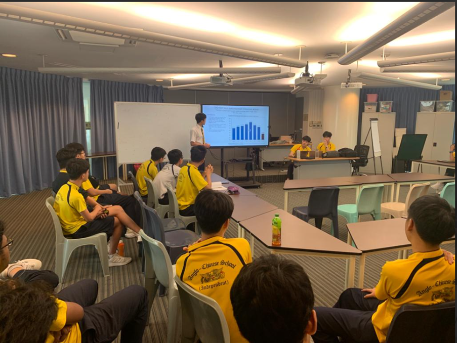ACS(I) NCC Sea cadets in yellow uniforms attend a briefing or presentation in a modern naval facility or command centre, with screens displaying information in the background.