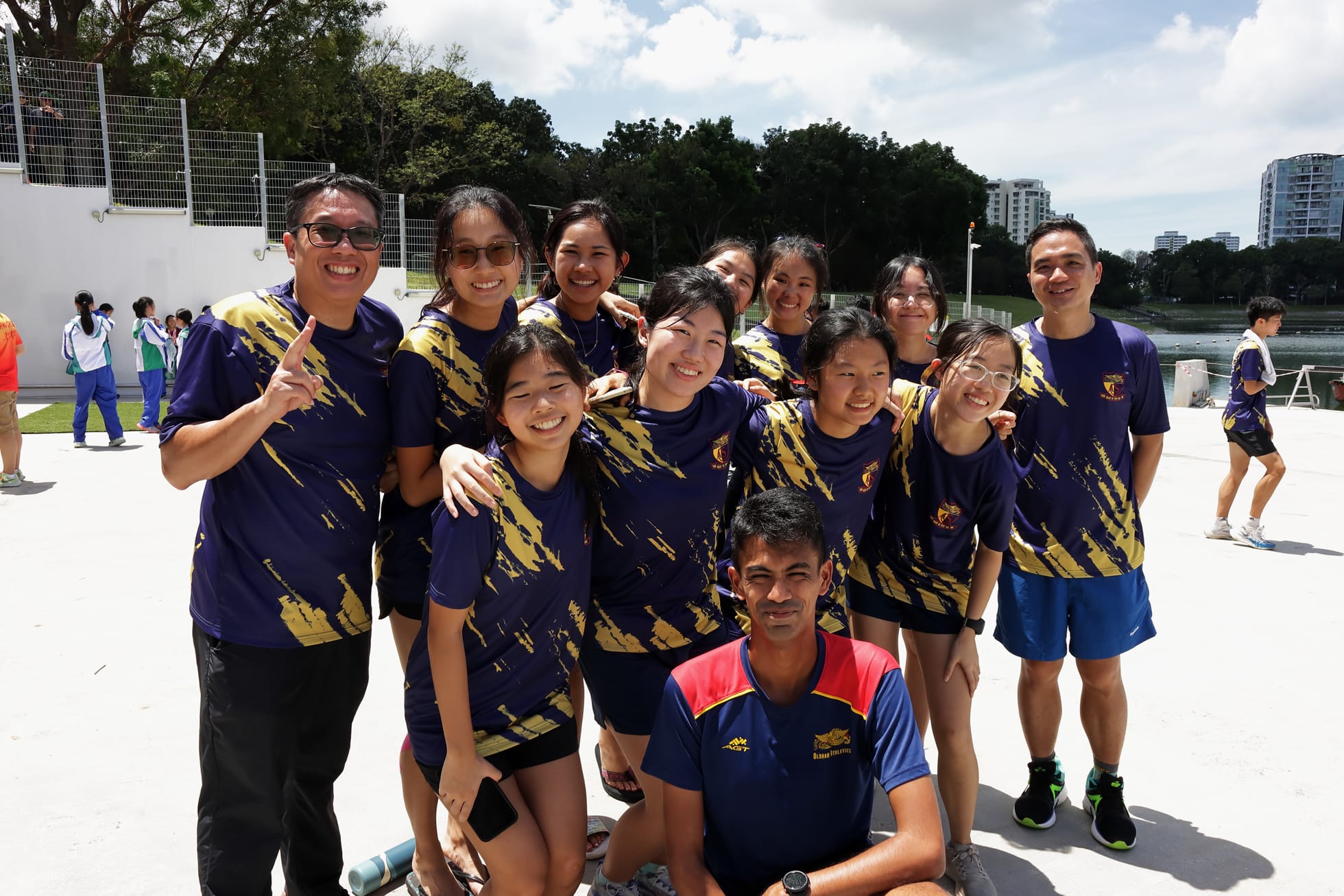 A group of about 12 people in matching purple and gold jerseys smiling outdoors near a waterway.