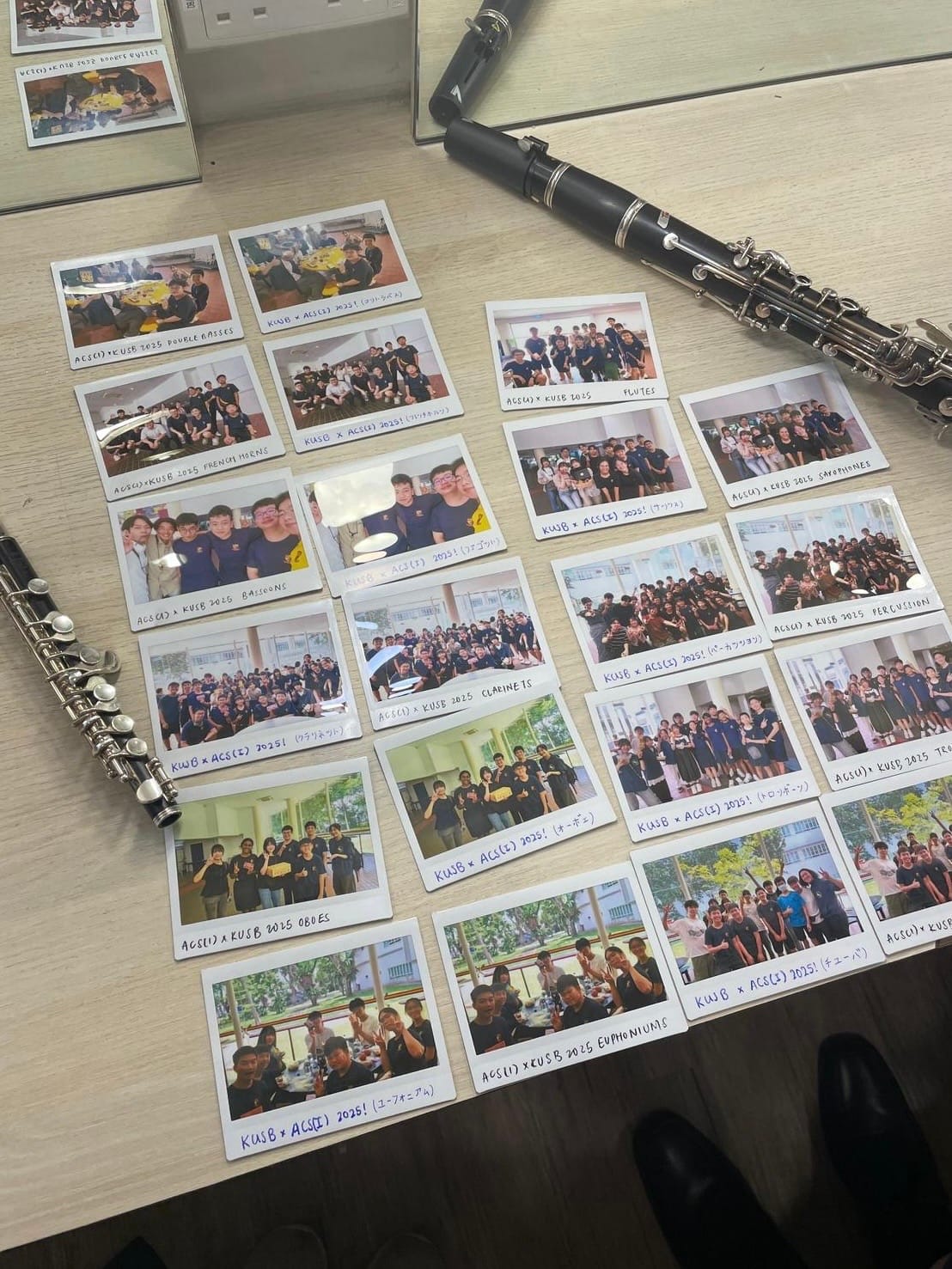 Polaroid photos of school band groups spread on a desk beside a clarinet and flute, labeled by instrument section.