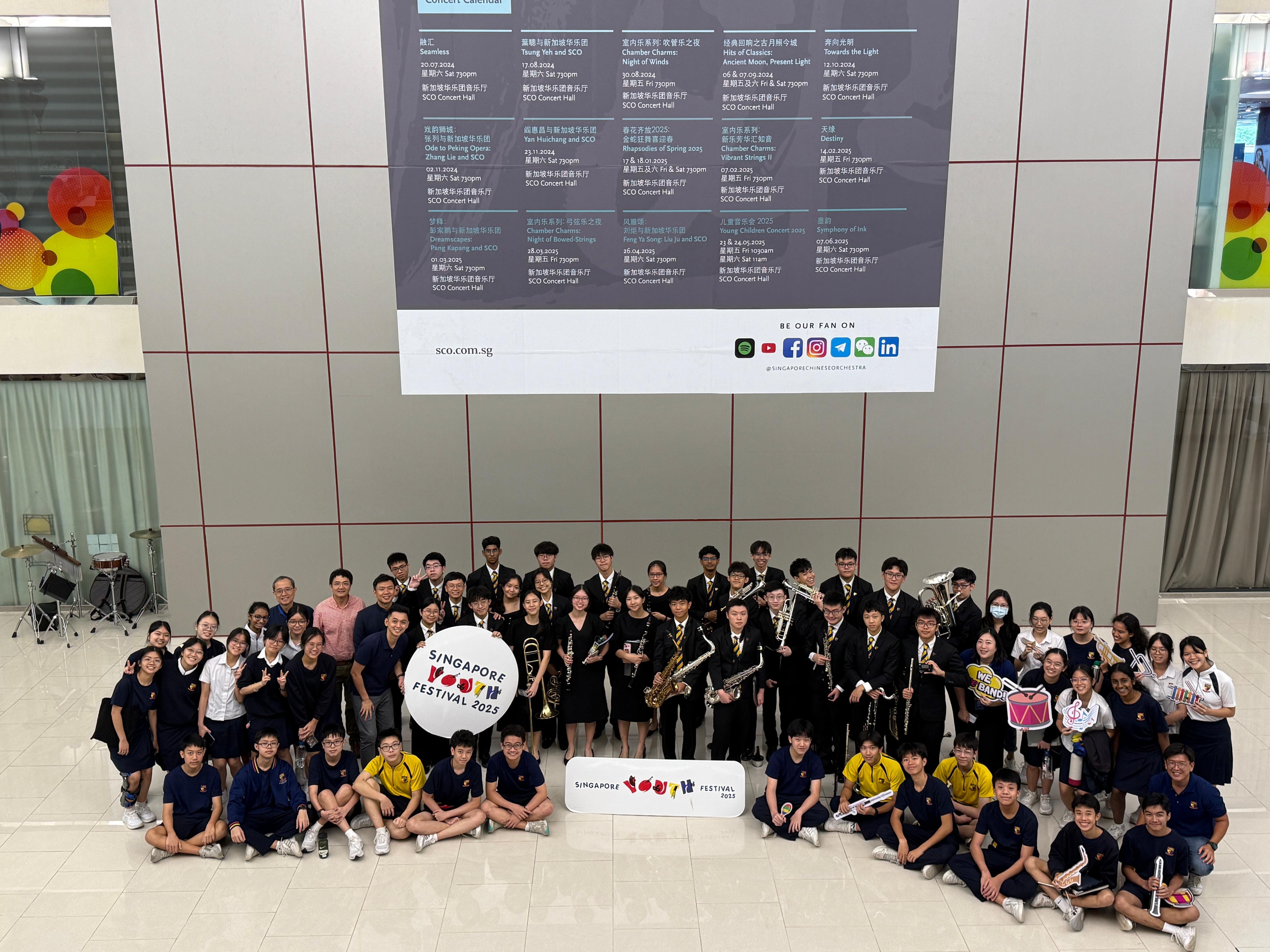 Large group of students with instruments posing for a photo at Singapore Youth Festival 2025 indoors.