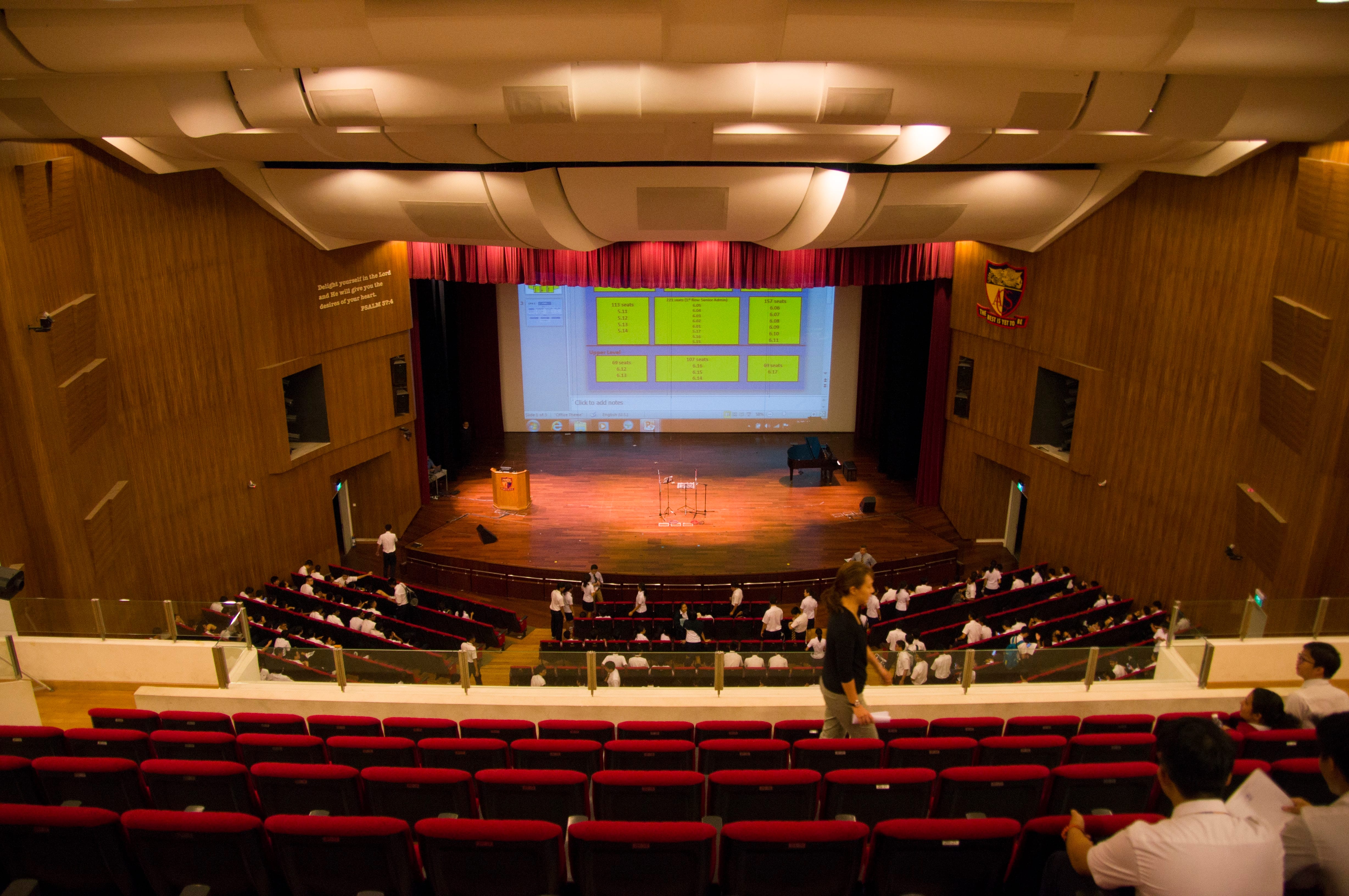 Empty theater auditorium with rows of red seats, multiple balcony levels, and warm overhead lighting.