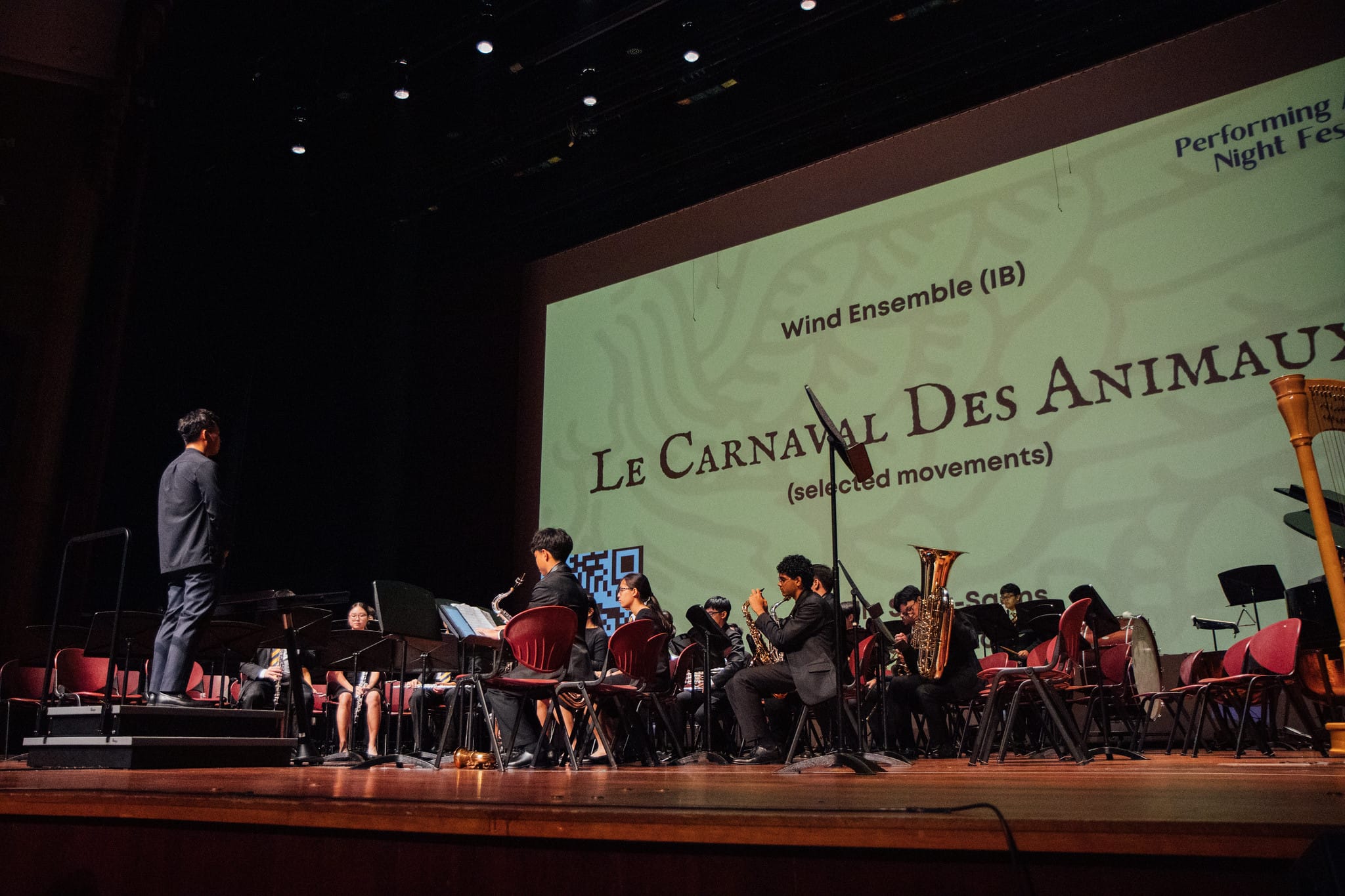 Wind ensemble students perform on stage with a conductor, screen behind them reads Le Carnaval Des Animaux.