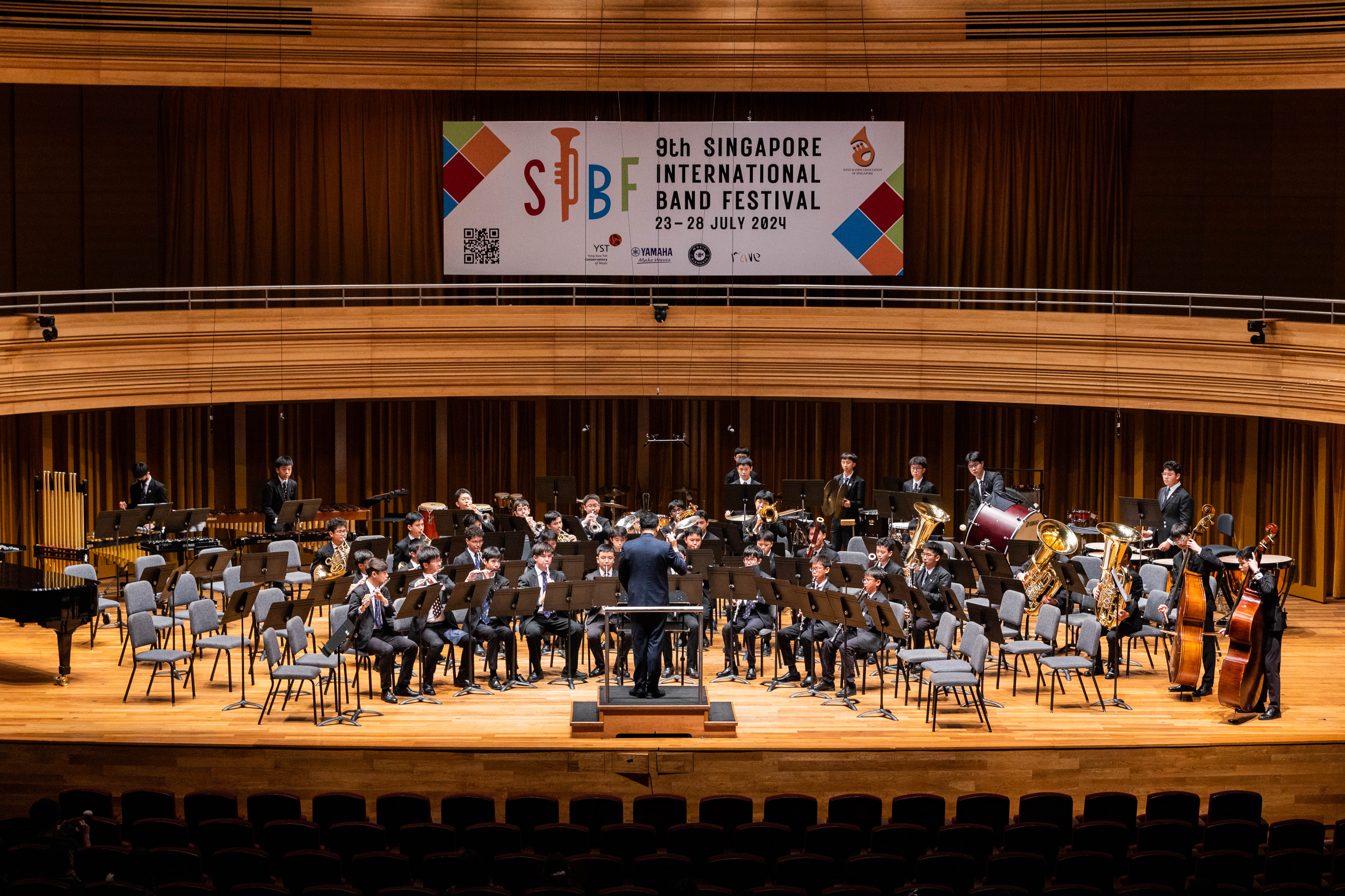 A band performs on stage at the 9th Singapore International Band Festival, July 23-28 2024, with a conductor leading.
