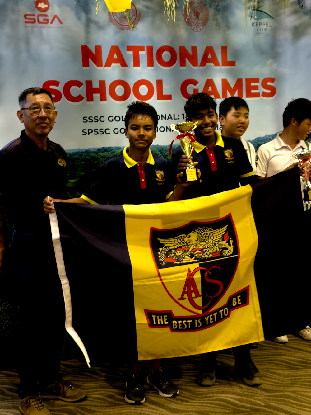 Students hold an ACS flag and trophy in front of a National School Games banner at Keppel Club.