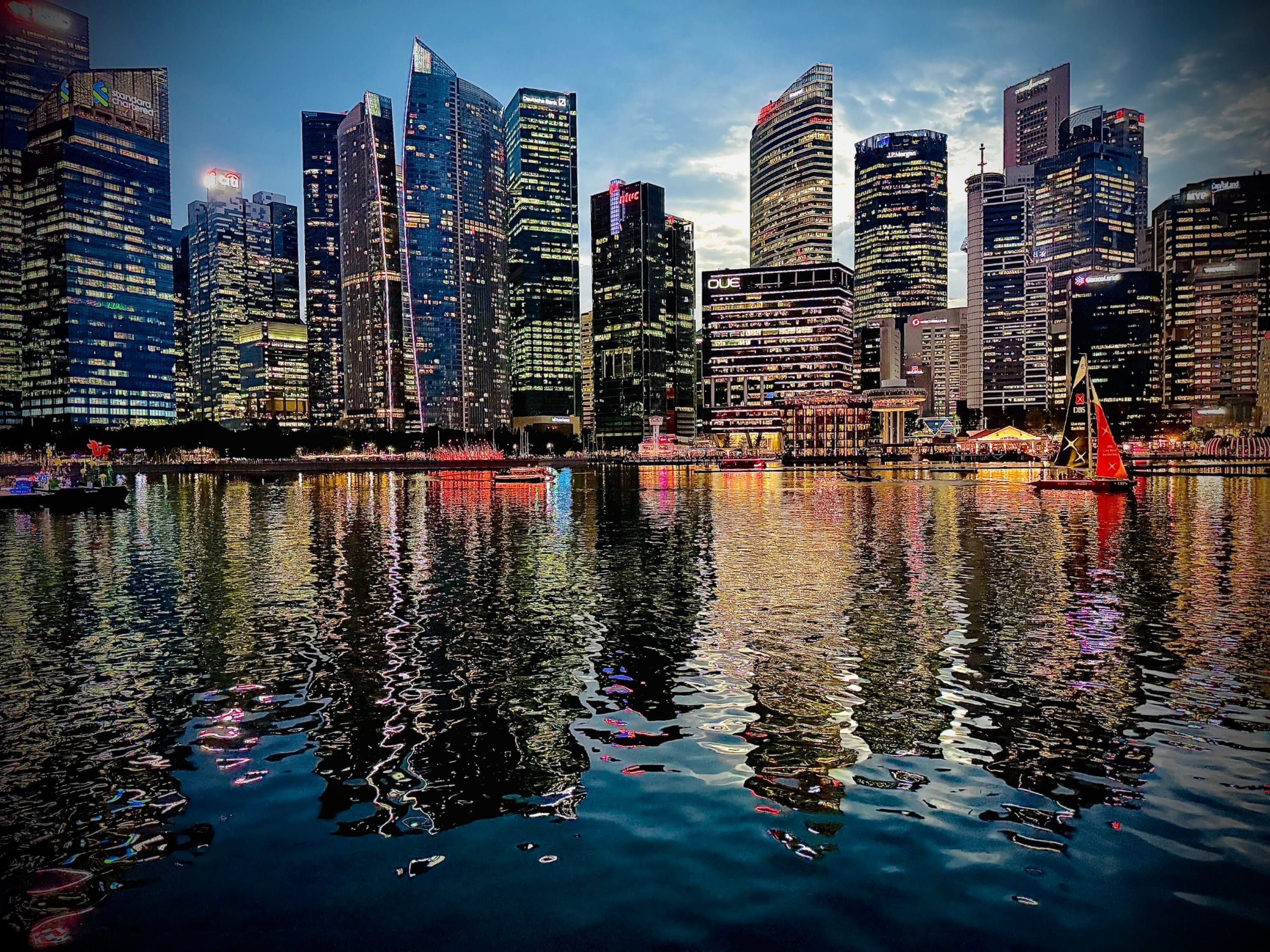 Singapore's Marina Bay skyline lit up at dusk with tall skyscrapers reflecting colorful lights on calm water.