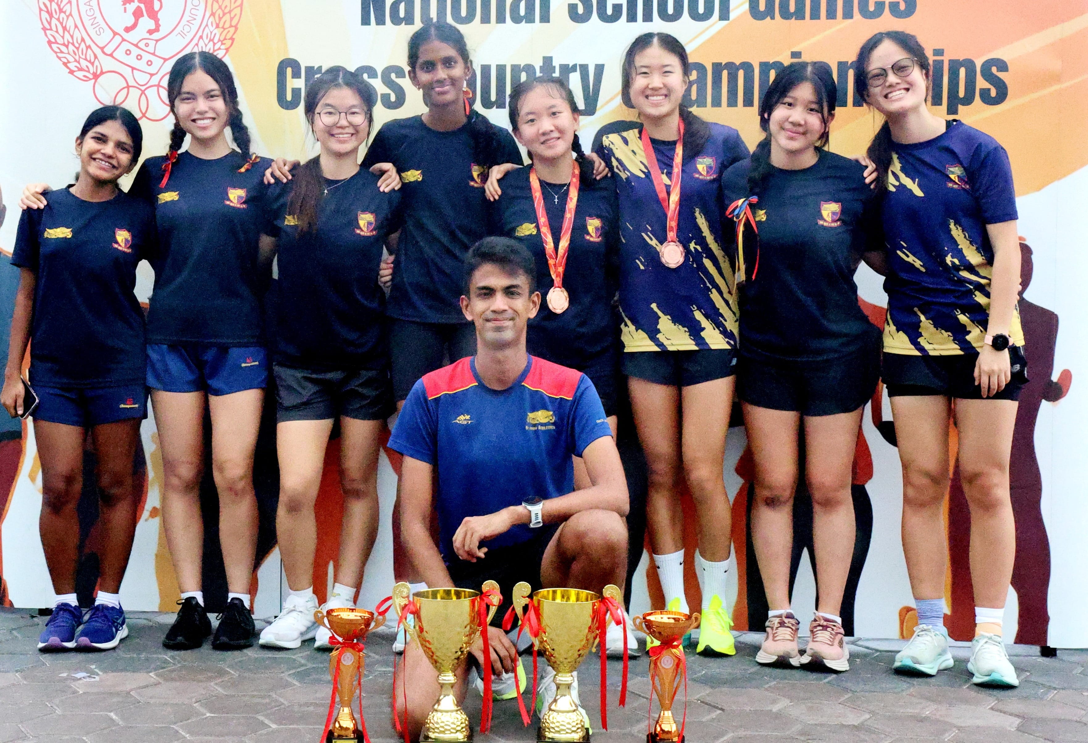 A school cross country team poses with gold trophies and medals at the National School Games Cross Country Championships.