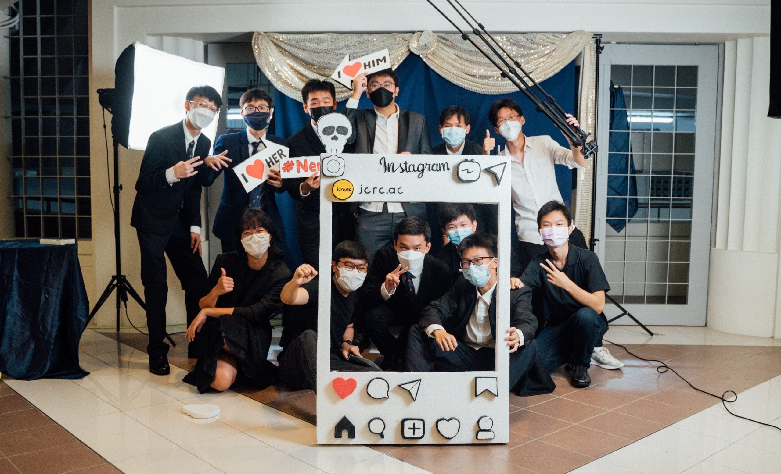 A group of masked people posing with a cardboard Instagram photo frame prop, holding fun signs at an event.