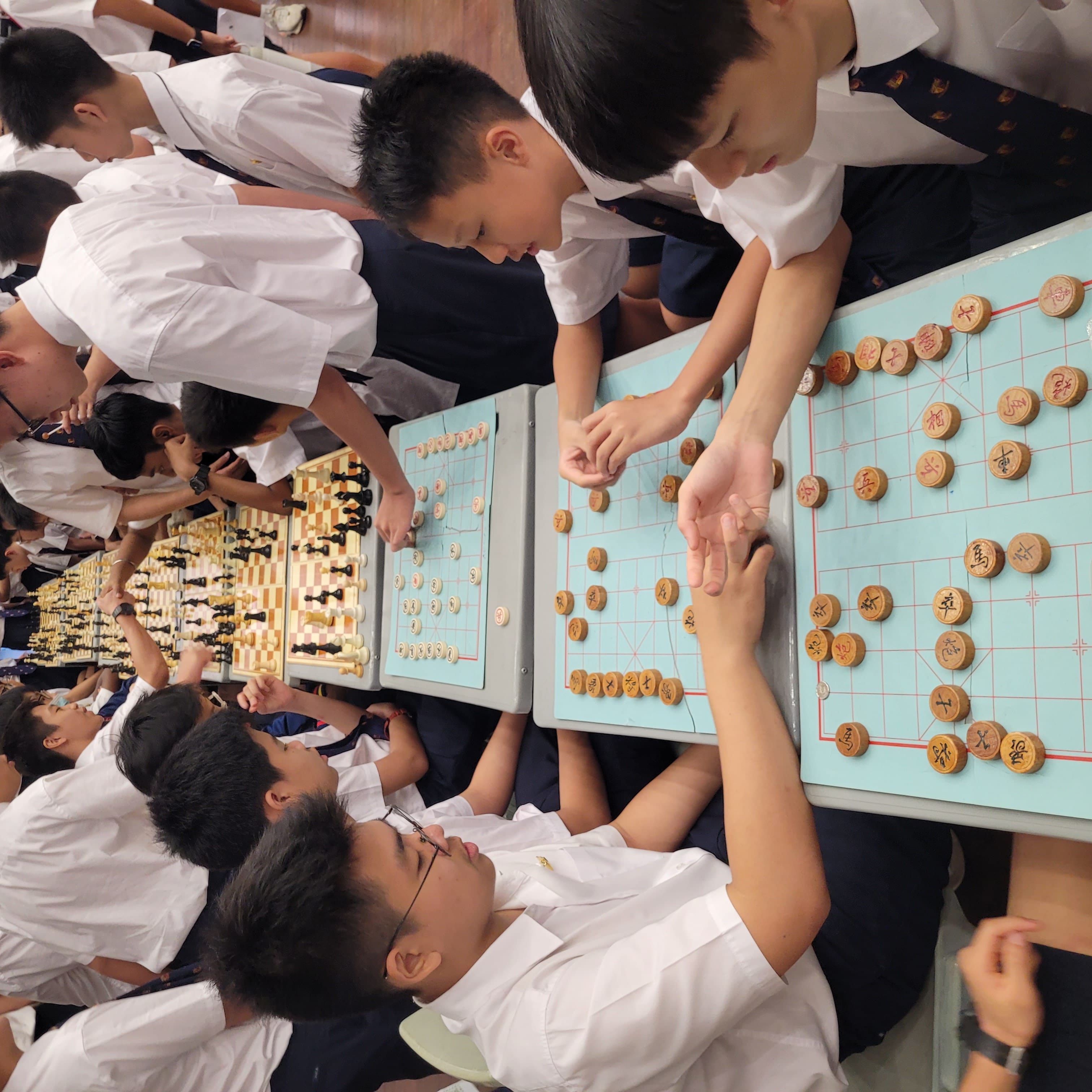 Students in white uniforms playing Chinese chess and Western chess at tables during a school tournament.