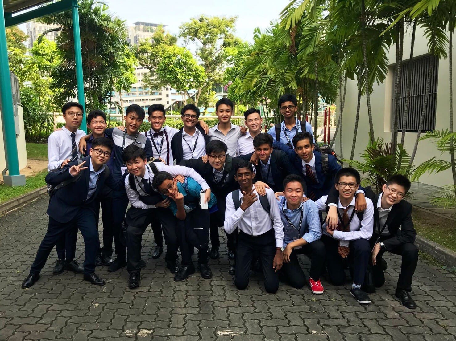 A large group of ACS(I) Young Diplomats Society members in formal attire poses for a group photo in a lush outdoor setting, likely at a MUN conference venue.