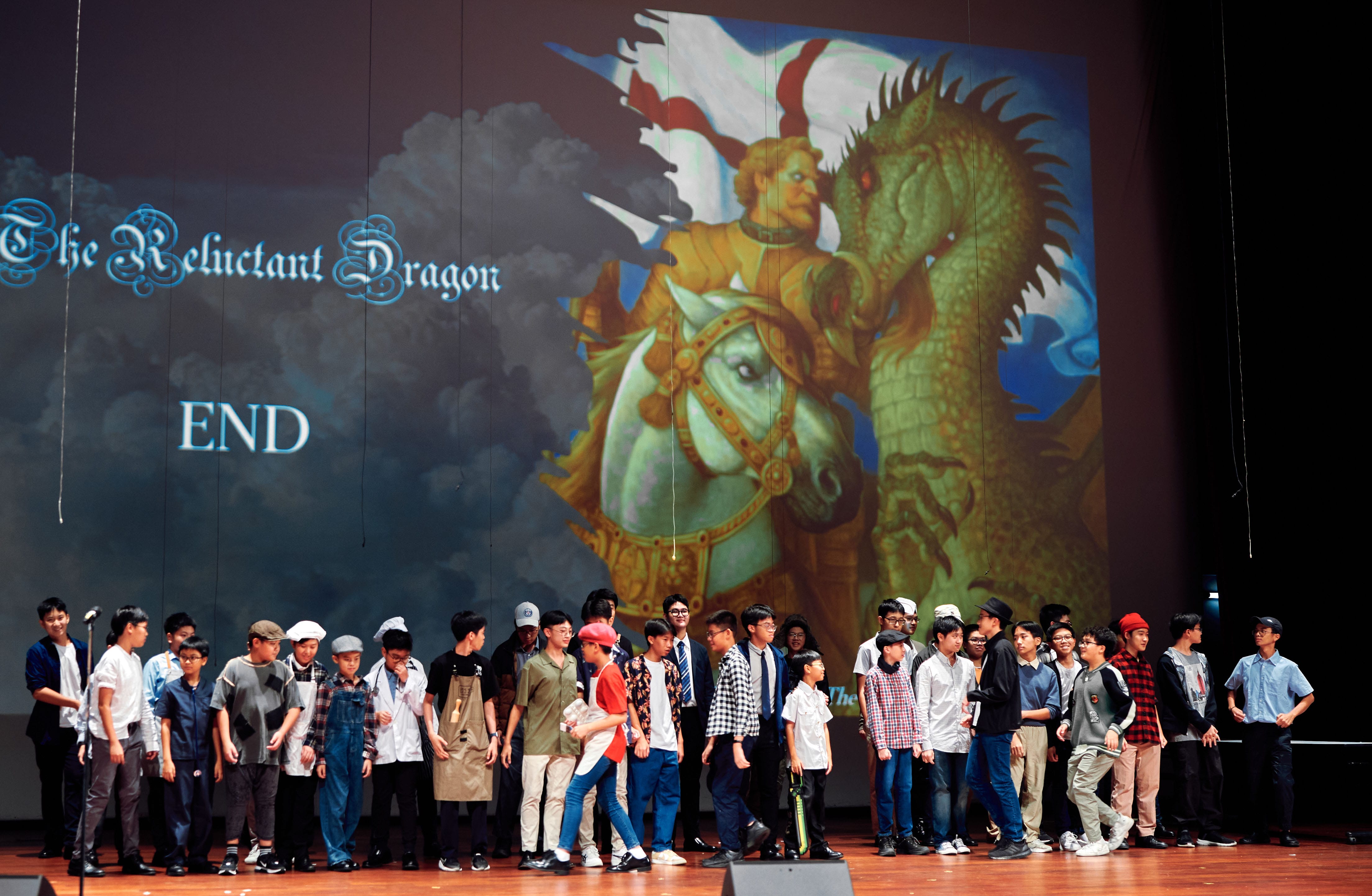A group of young students stand on stage at the end of a school play called The Reluctant Dragon.